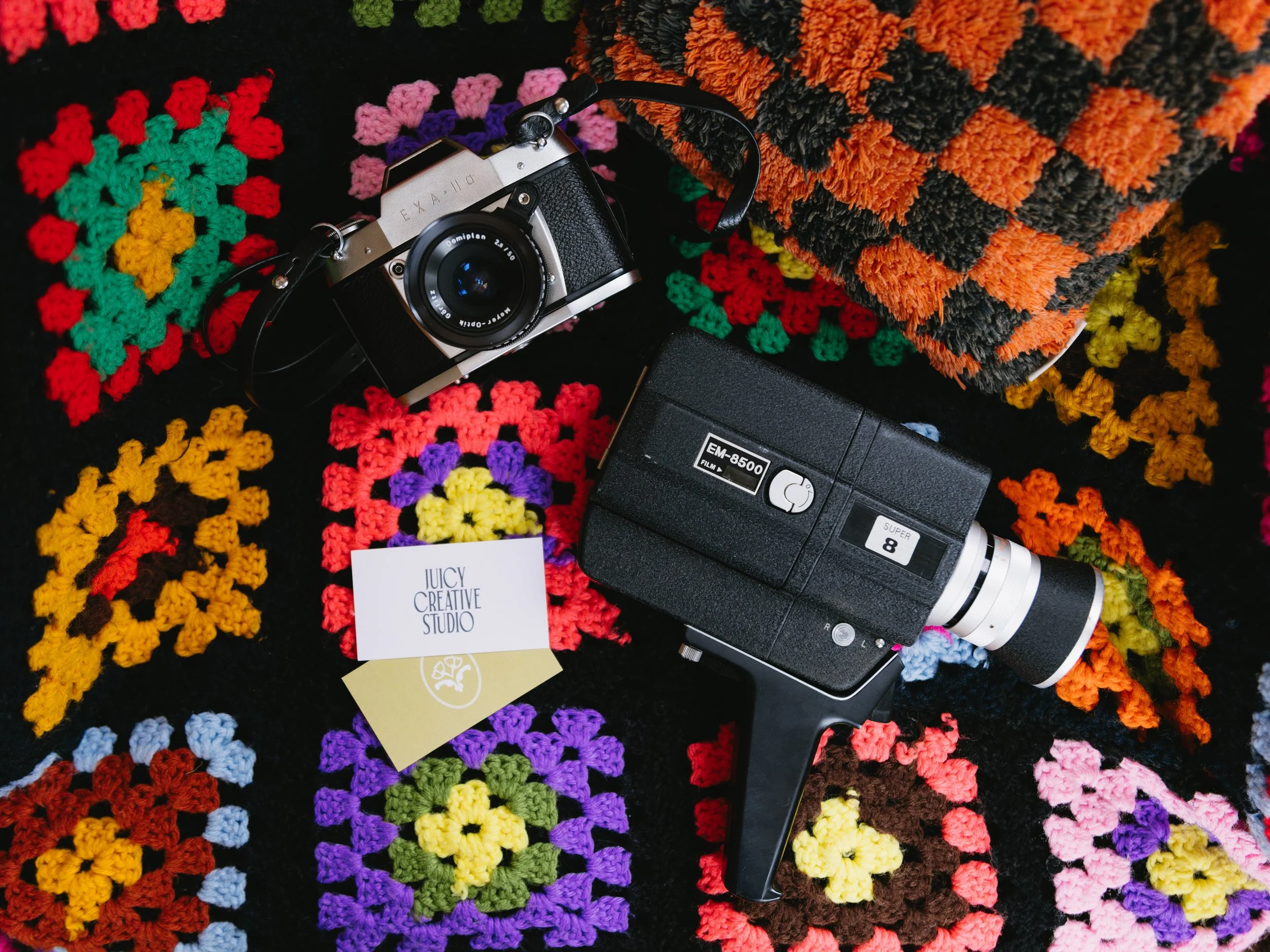 A vintage film camera, a video camera, and a crocheted blanket with colorful granny squares.