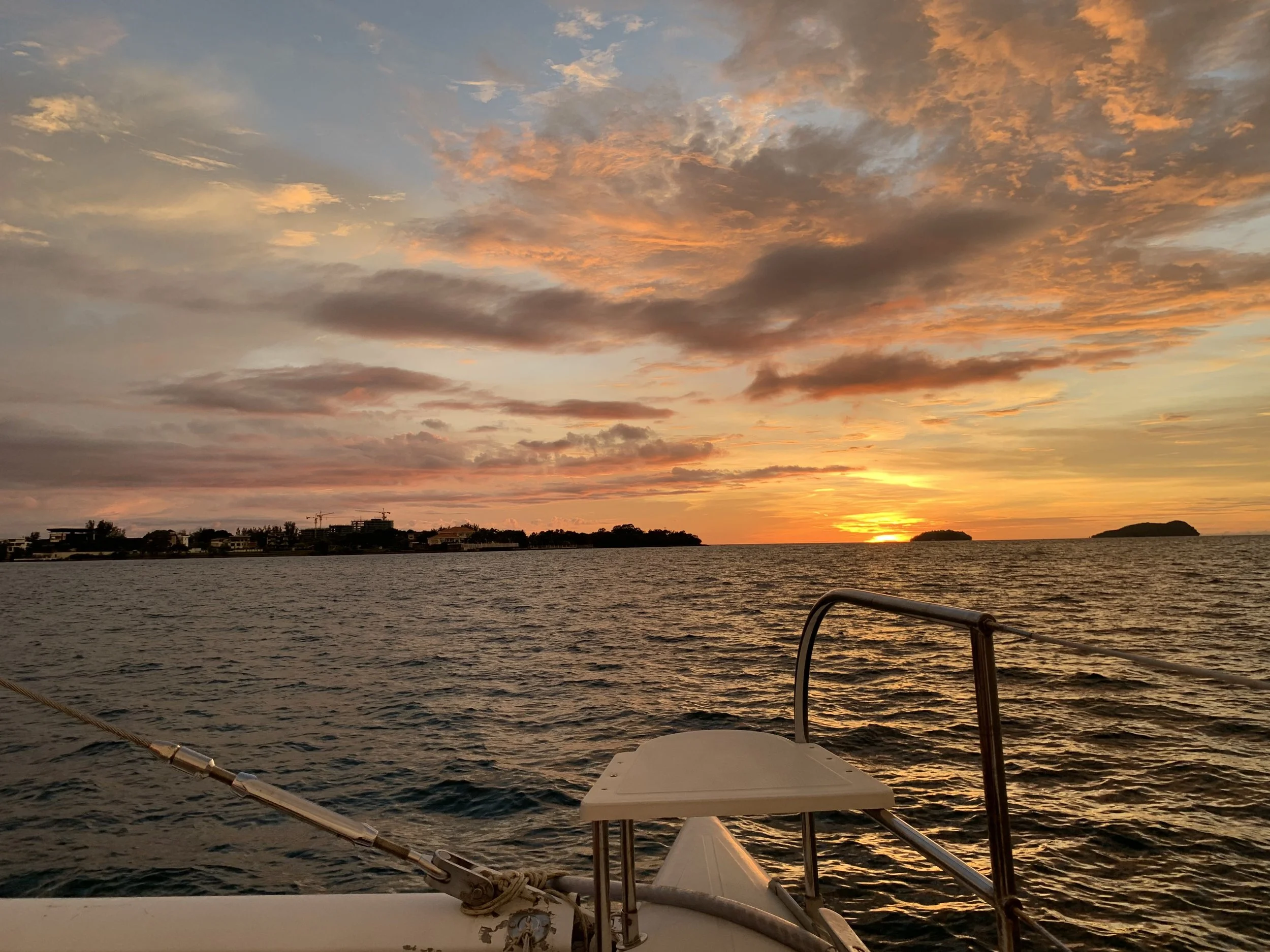 Sunset over the water from a boat with part of boat and railing in the foreground.