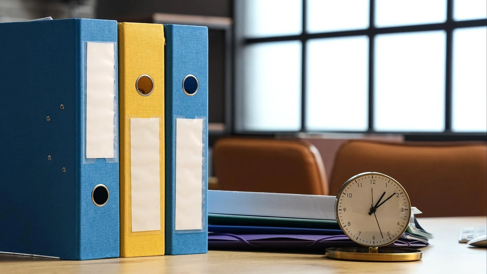 Blue and yellow office binders beside stacked folders and a desk clock.