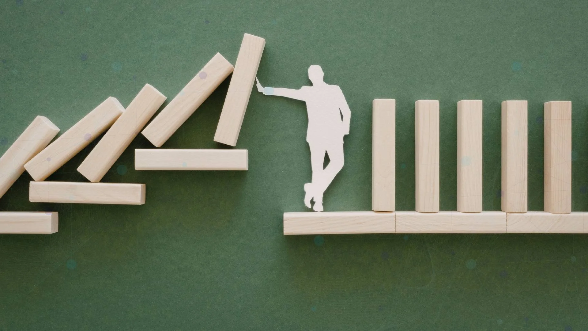 Paper figure holding back falling wooden blocks beside a stable row of upright blocks.