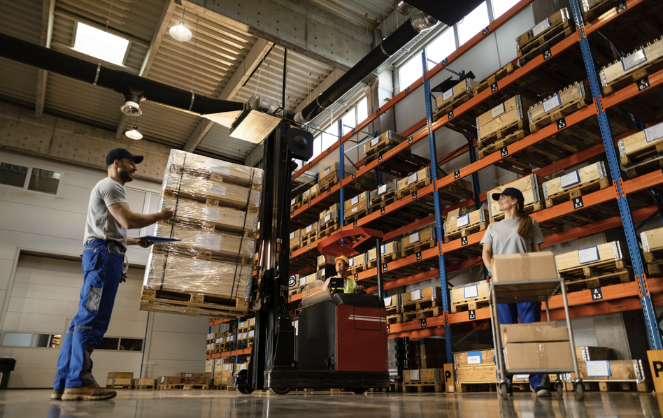 Warehouse workers using forklift and carts to handle pallets on industrial shelves.