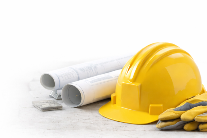 Yellow construction hard hat, rolled-up blueprints, gloves, and a small container on a white background.