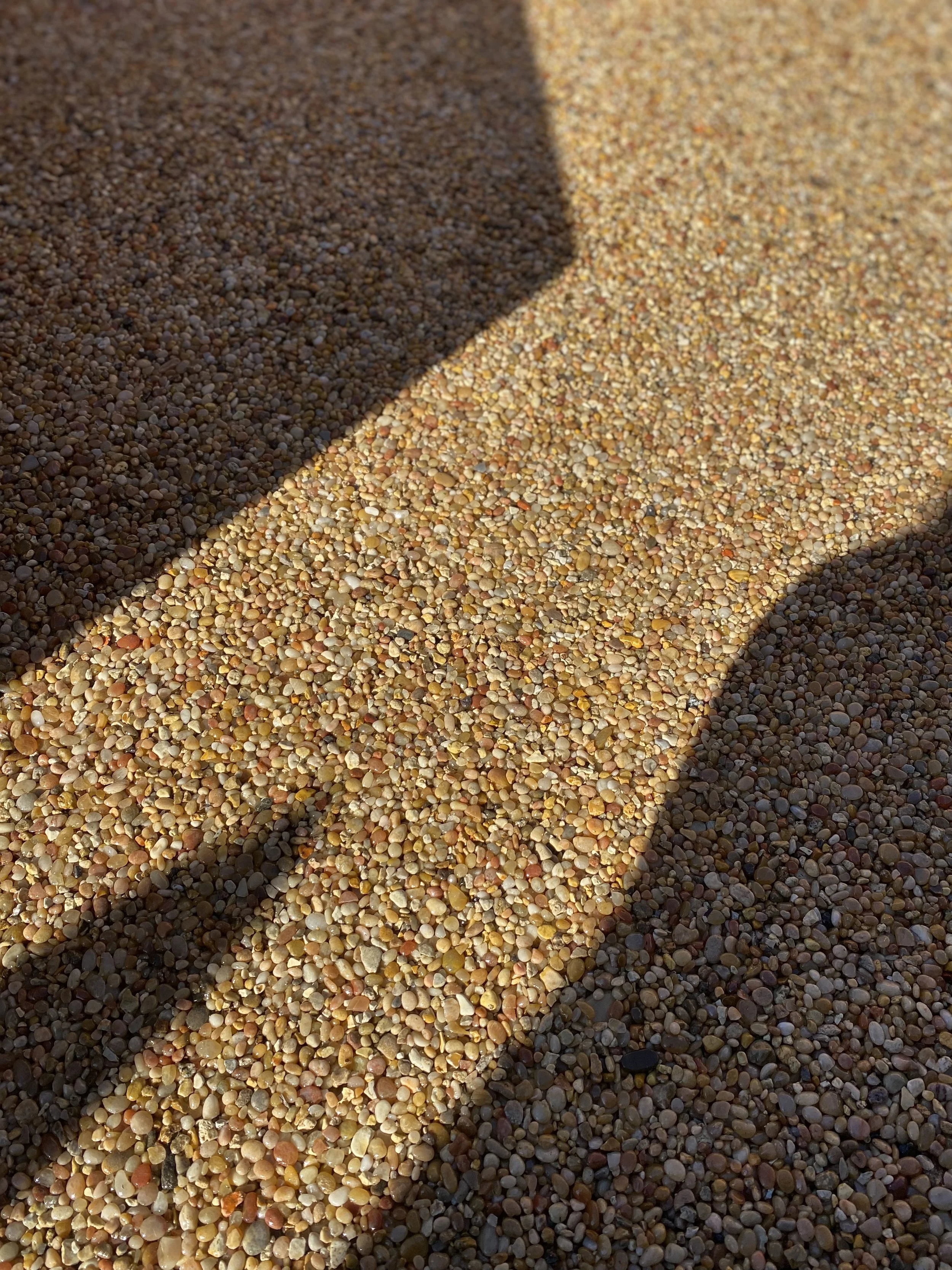 Close-up view of a beach with multicolored small pebbles, partially shaded by shadow.