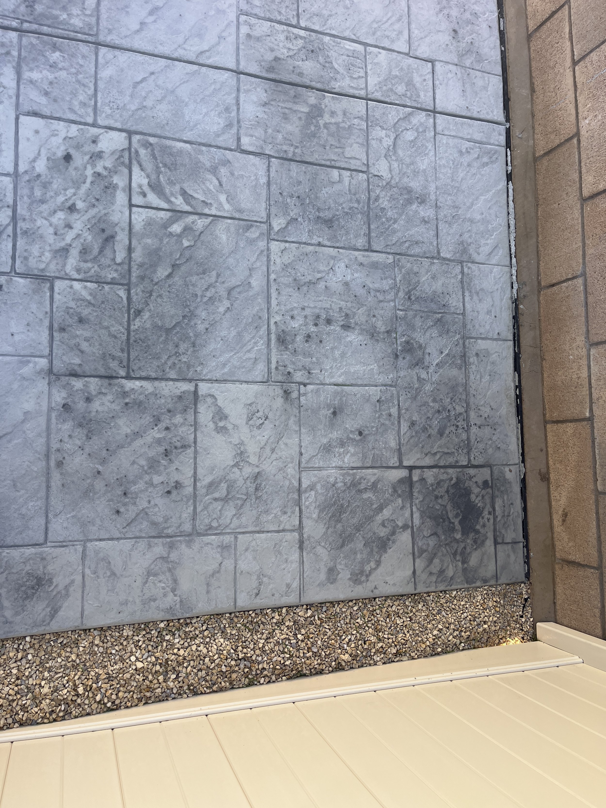 Close-up of a gray stone tile floor next to a strip of brown gravel and a white vinyl wall.