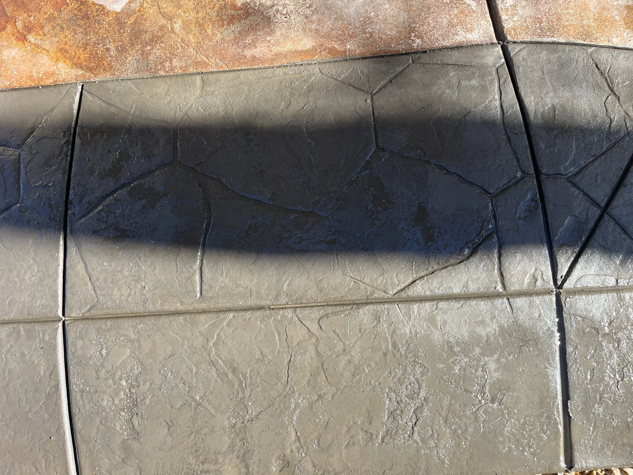 Close-up of decorative stone or tile flooring with darker and lighter sections, featuring a shadow cast across the surface.