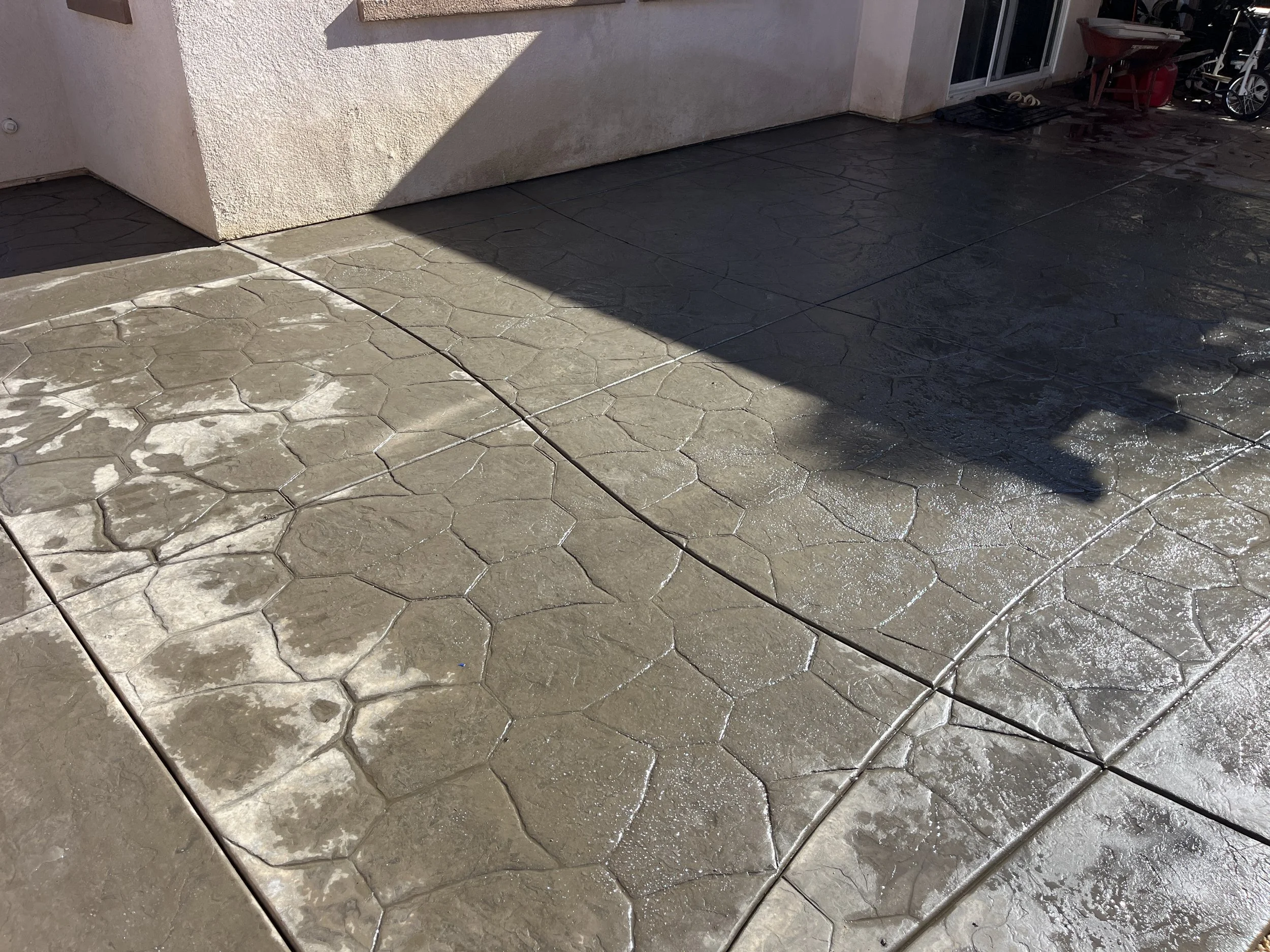Two attached concrete patio sections with a hexagonal pattern, wet on the right side and dry on the left side, next to a building wall.