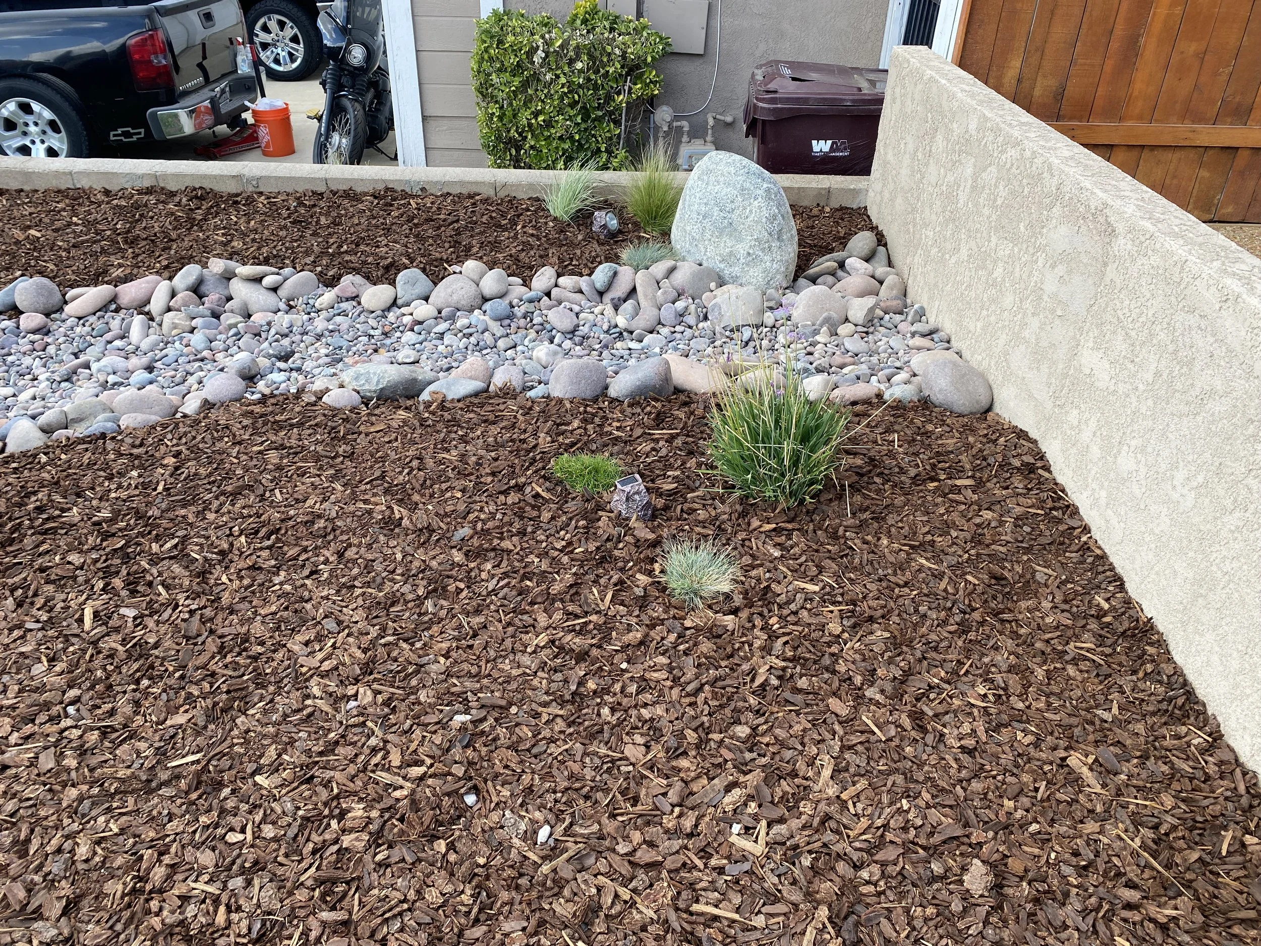 A landscaped garden area with brown mulch, decorative rocks, a concrete wall, and small plants, located near Temecula