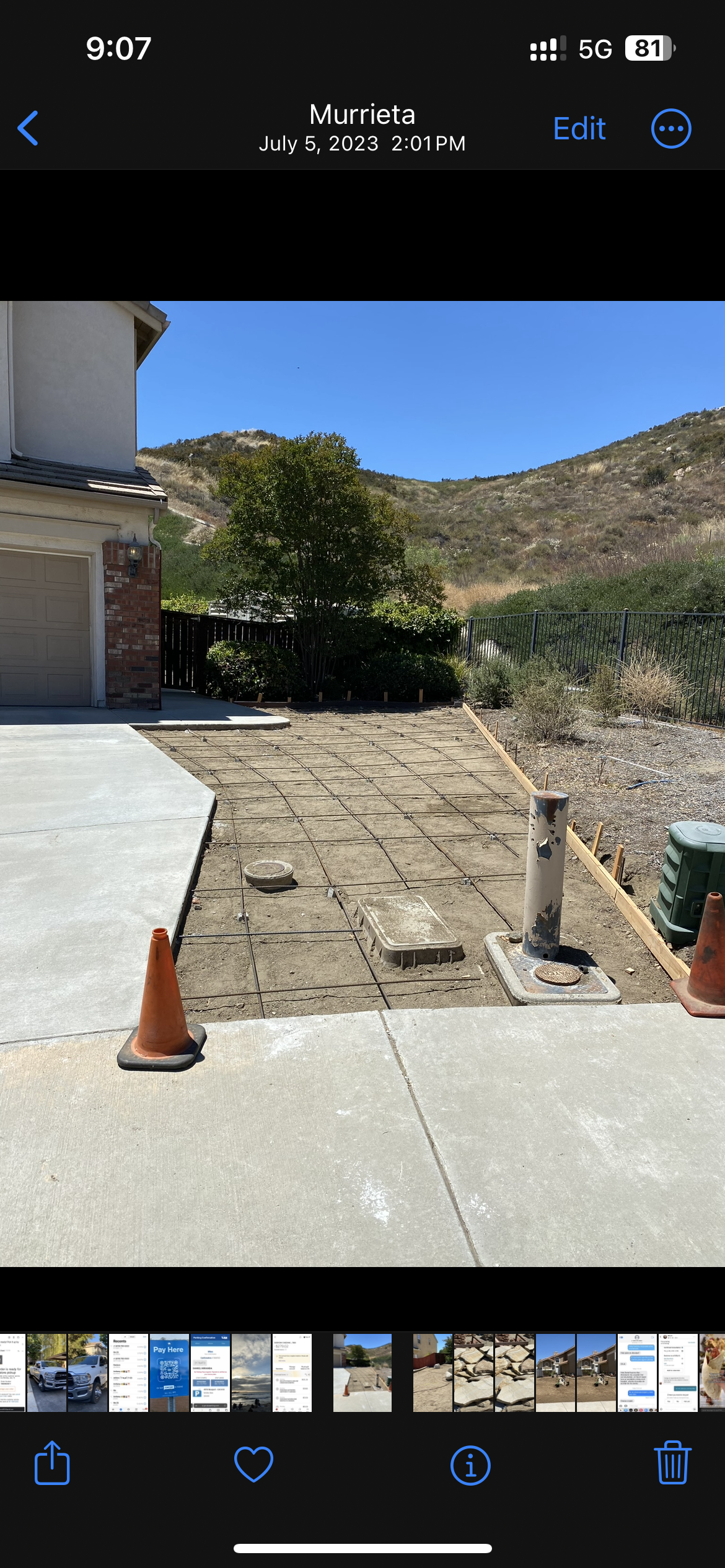 Front yard under construction with exposed soil, metal rebar grid, traffic cones, and utility poles, with a house and mountains in the background.