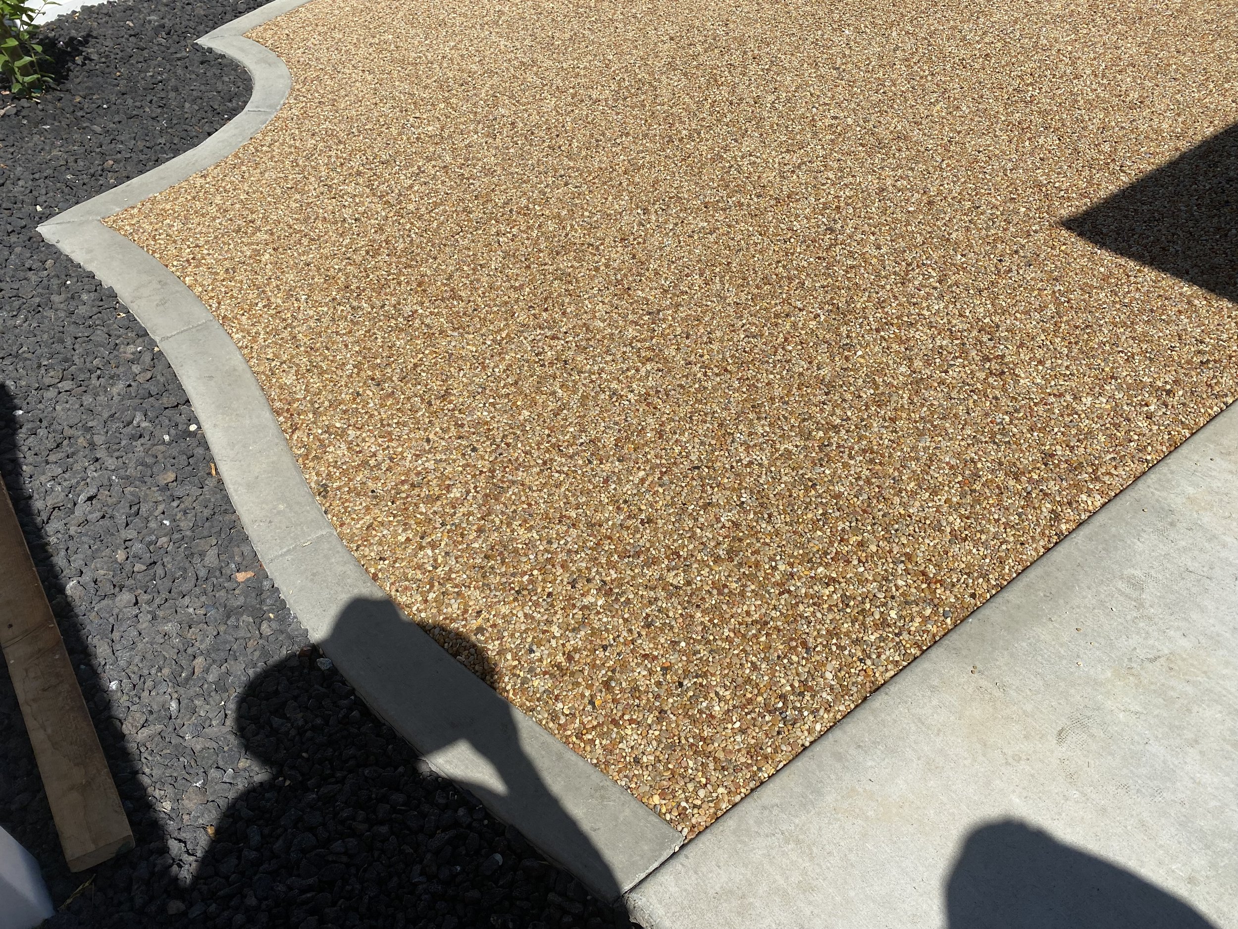 Close-up view of a gravel pathway with a concrete border, shadow cast on it from a nearby structure.