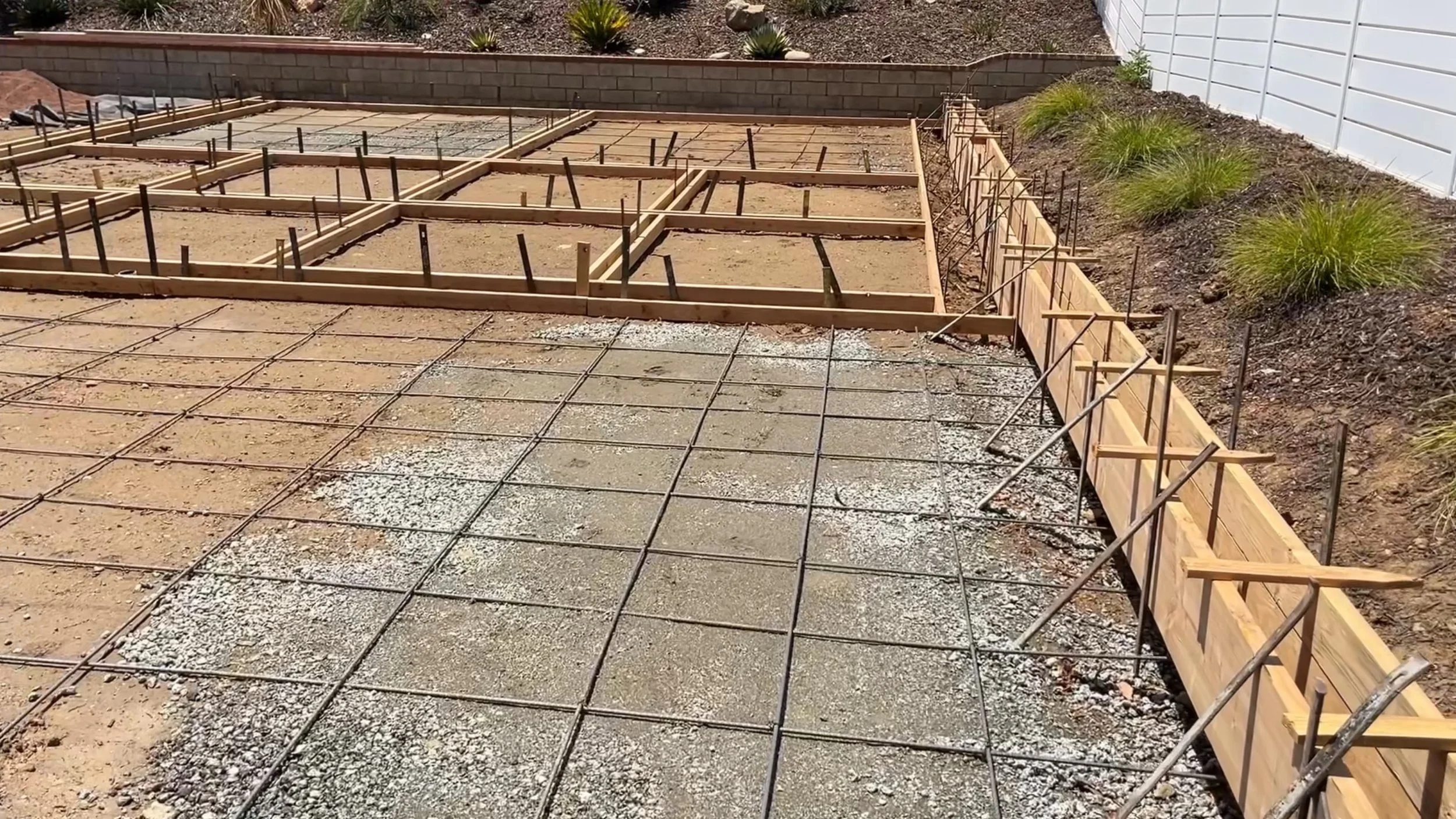 Construction site with concrete foundation, metal rebar grid, and wooden framing for a new building.