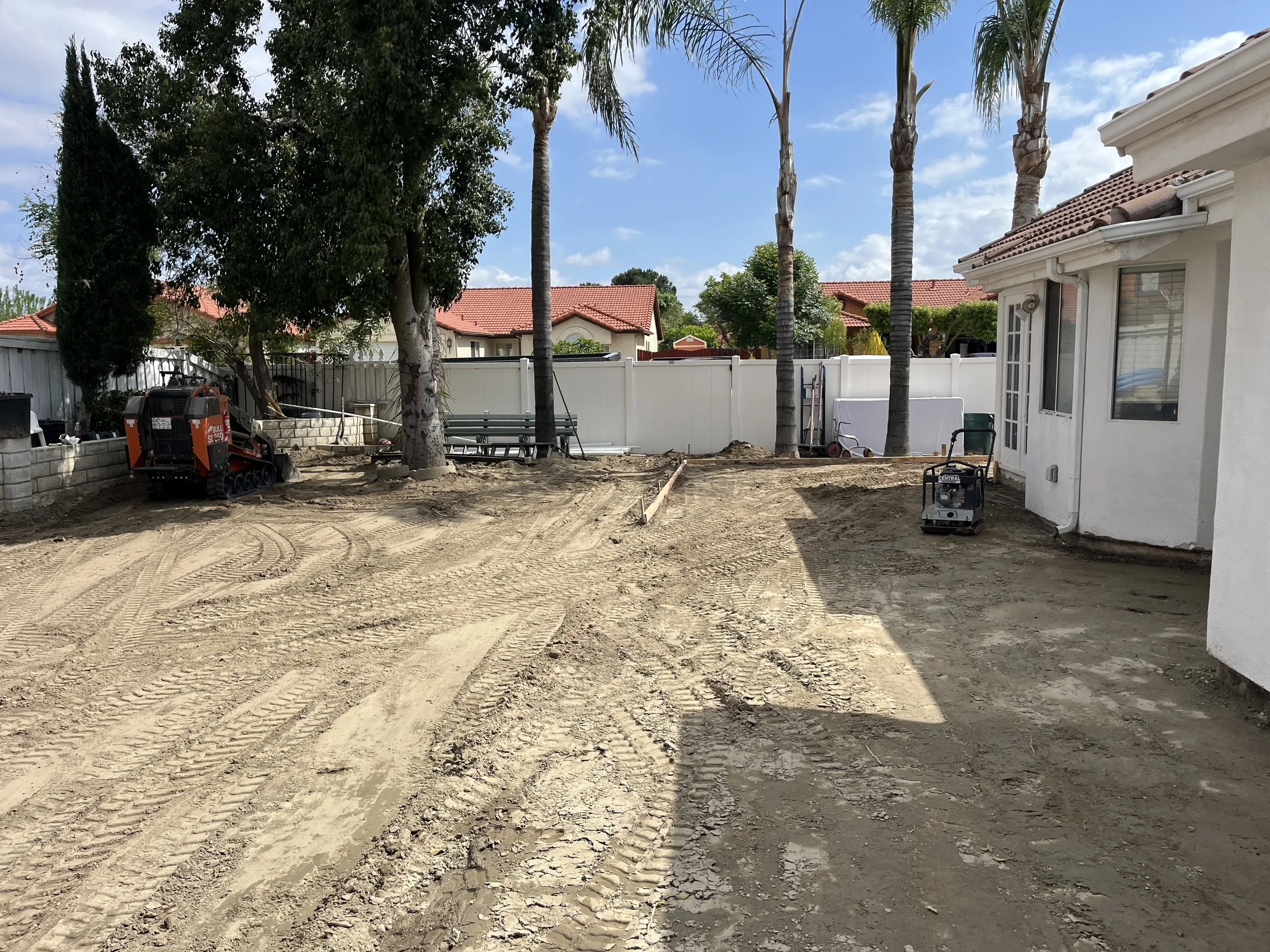 Backyard undergoing landscape or patio renovation with exposed dirt and construction equipment.