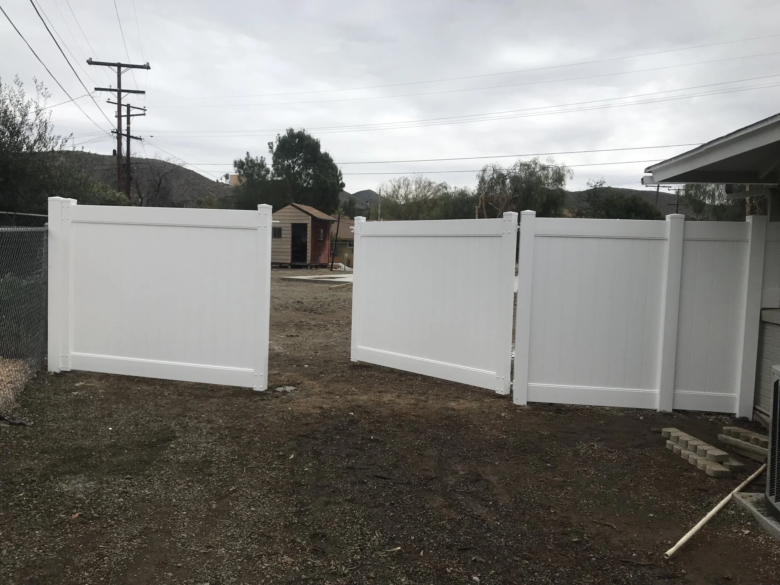 A white vinyl fence with lattice top panels on a residential property, with a cloudy sky and utility poles in the background.