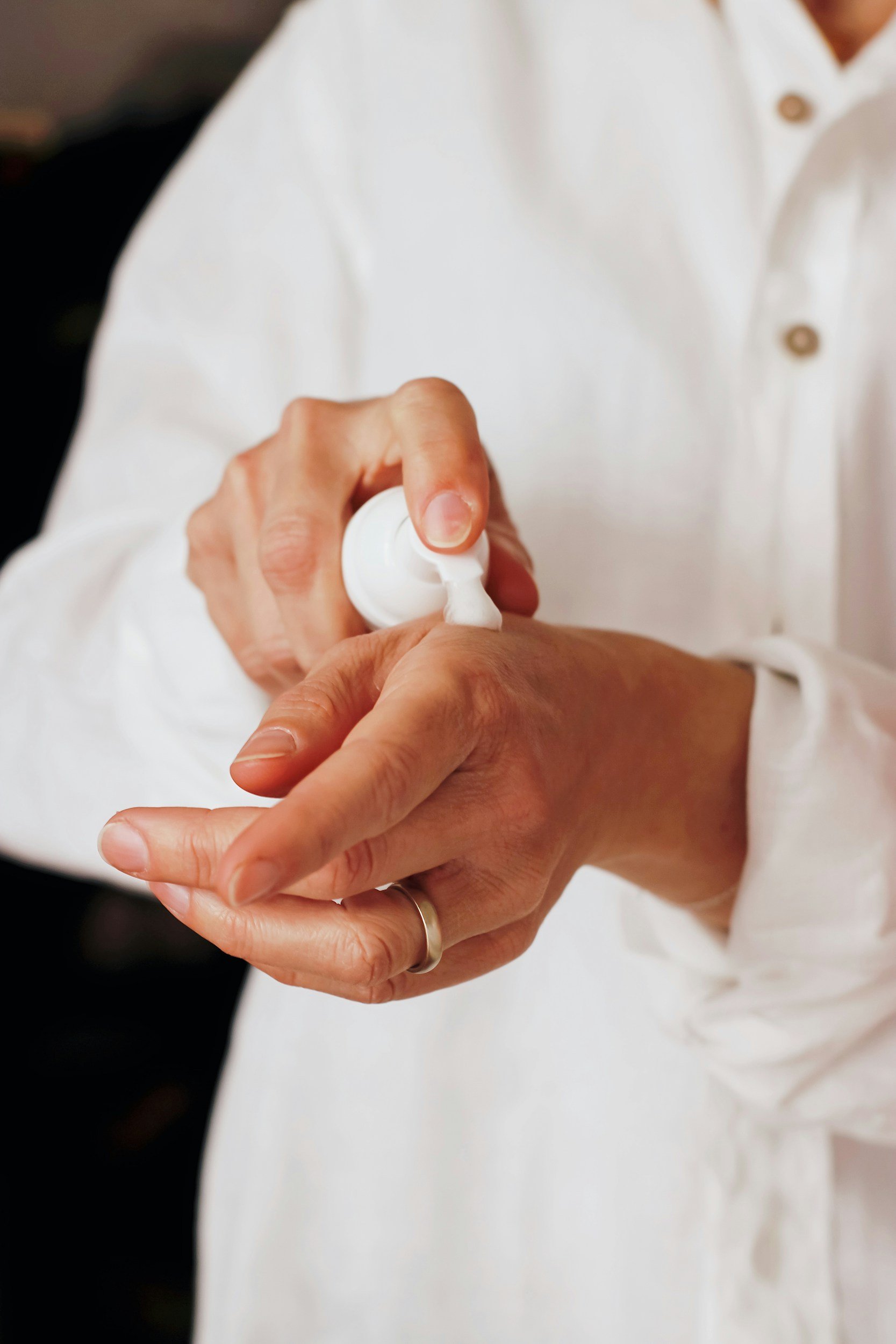 Person with a white shirt applying hand sanitizer onto their hands.