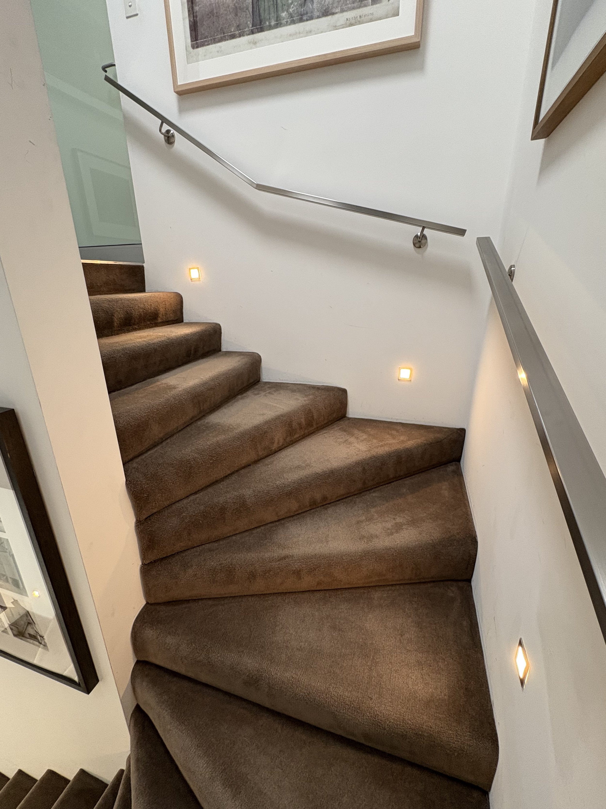 Indoor staircase with brown carpet, metal handrails on both sides, and wall-mounted lights.
