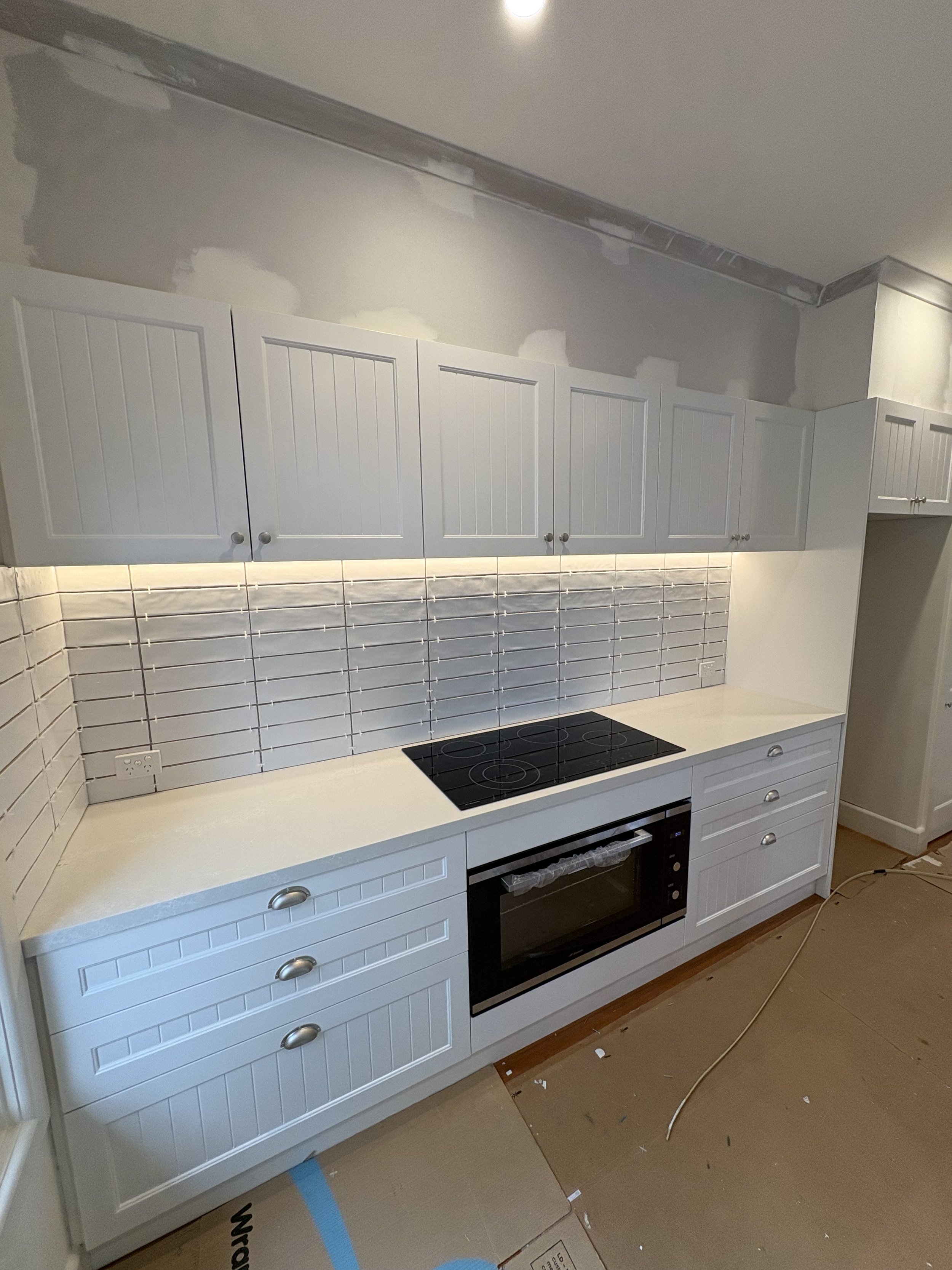 Kitchen with white cabinets, tiled backsplash, and a black stovetop, in a space under renovation.
