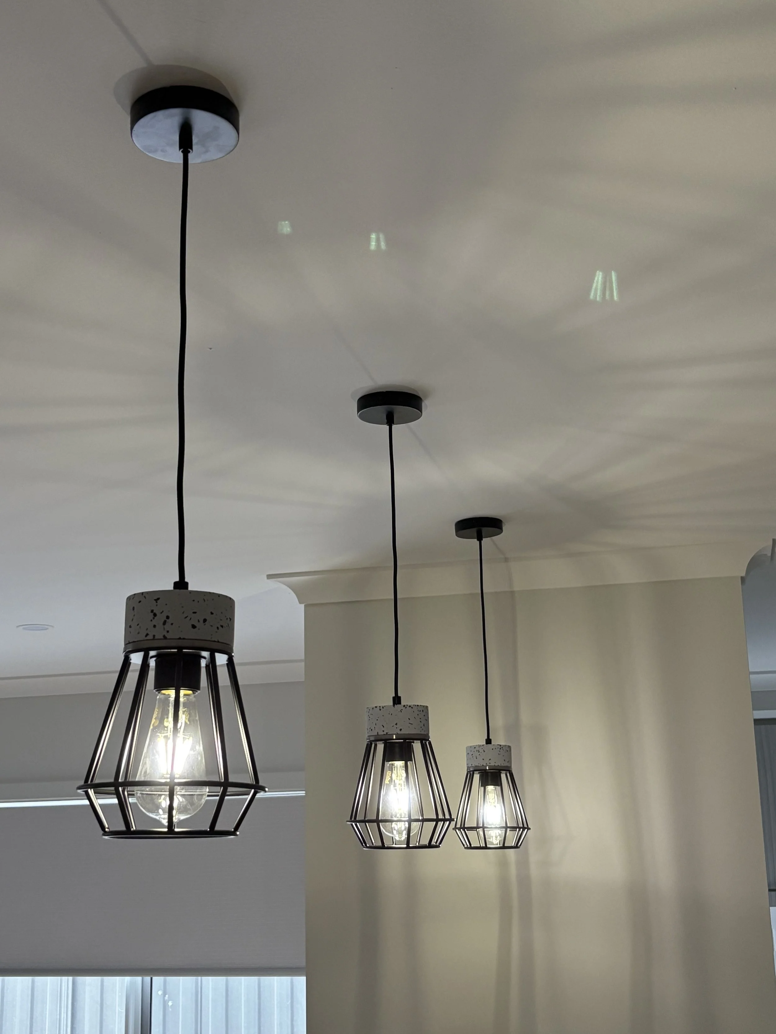 Three pendant light fixtures with transparent bulbs and black metal frames hanging from black cords from a white ceiling.