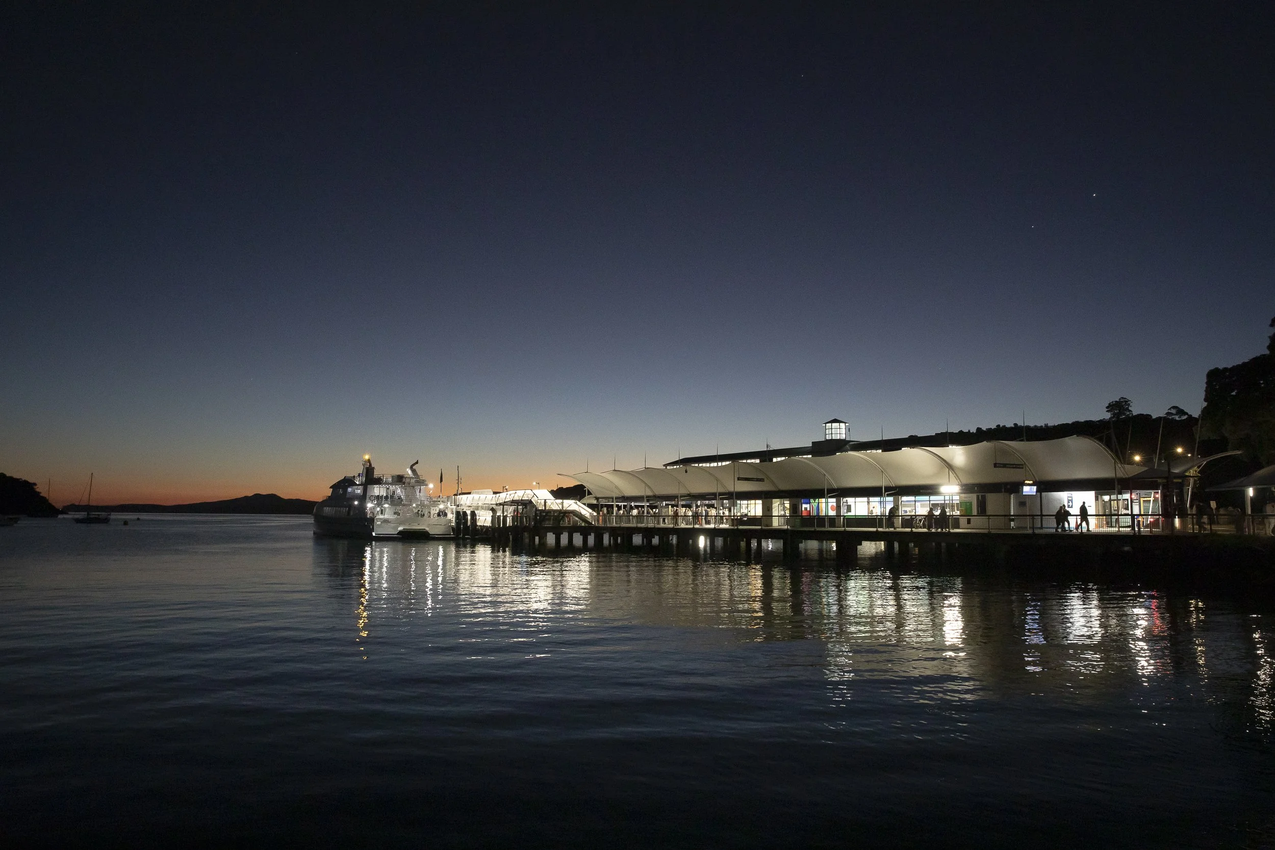 Matiatia Bay Ferry Terminal on Waiheke Island with and a clear night sky with stars reflected on the water.
