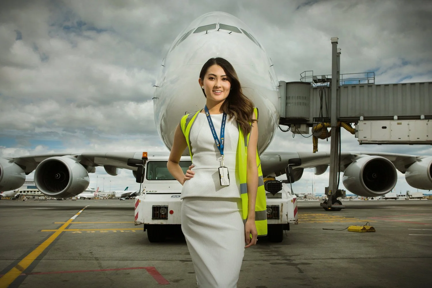 A woman in a white dress and yellow safety vest standing in front of an airplane on the tarmac at an airport.