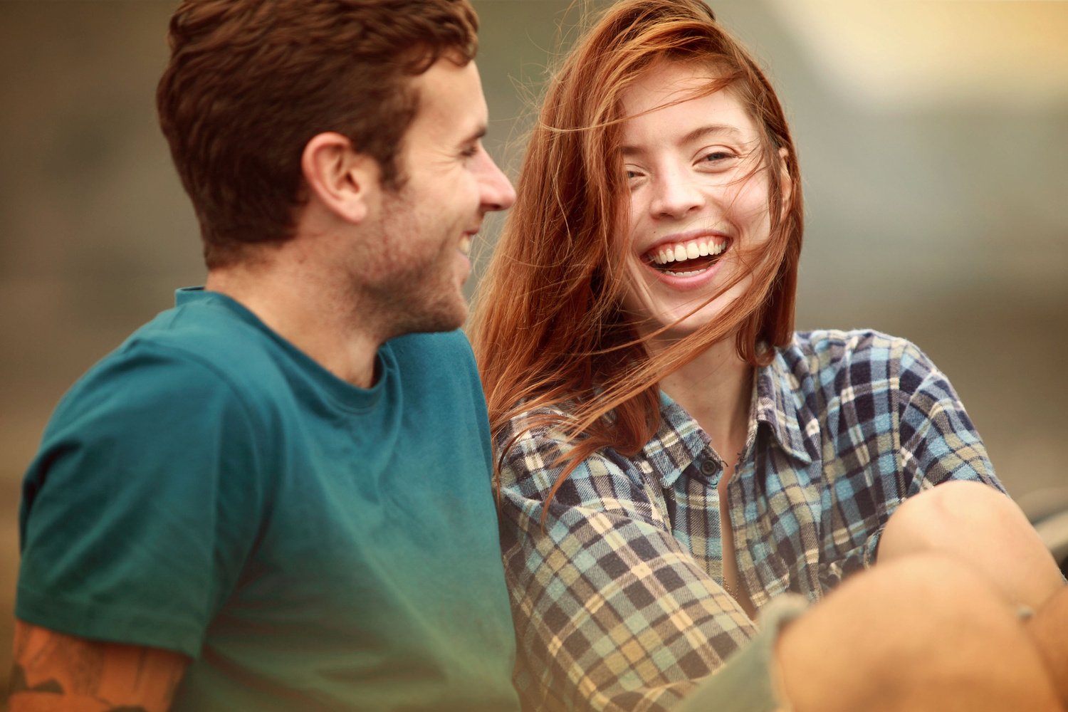 A man and a woman outdoors, smiling and laughing at each other.