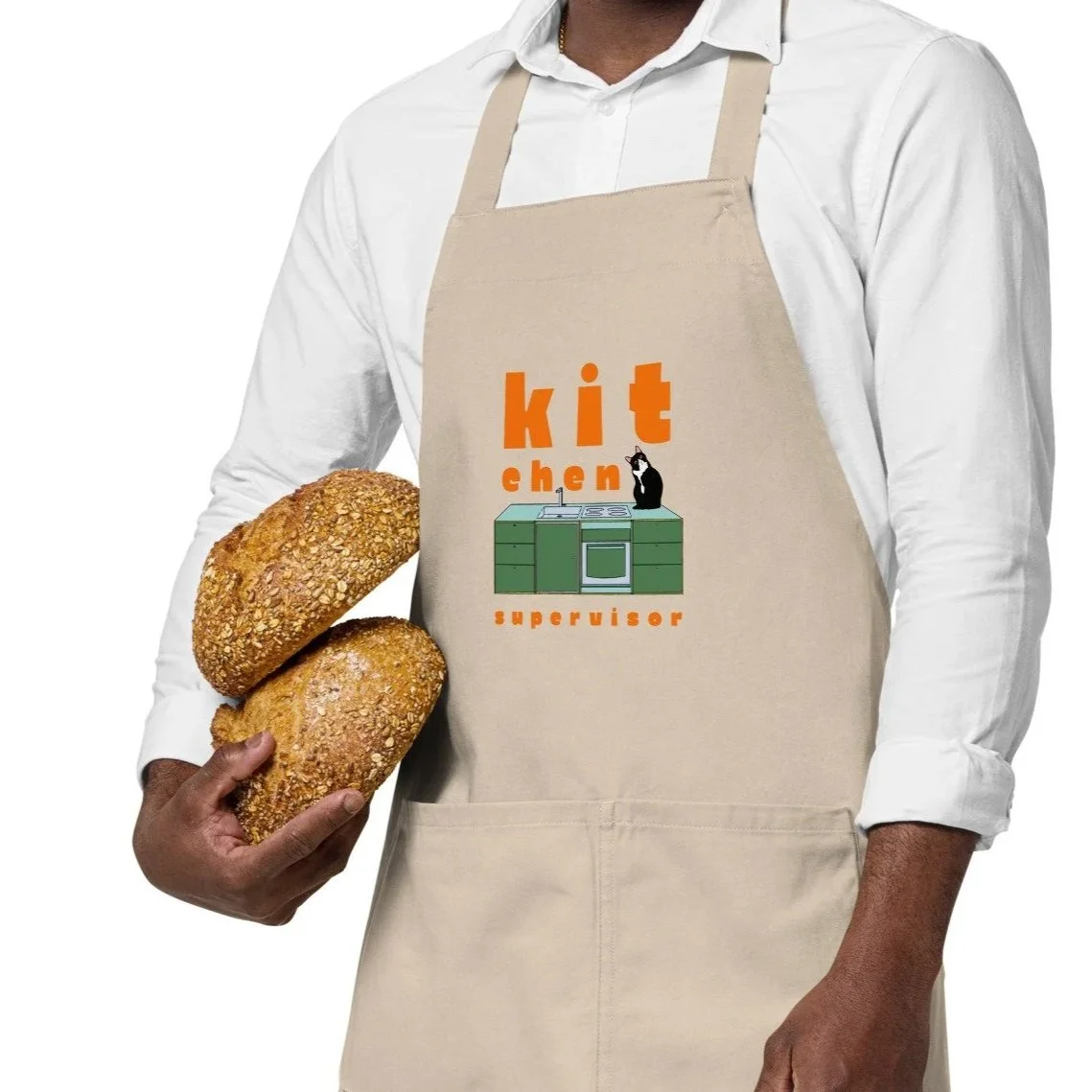 A person wearing a beige apron with the words 'kitchen supervisor' and a graphic of a kitchen with a cat, holding two loaves of bread.