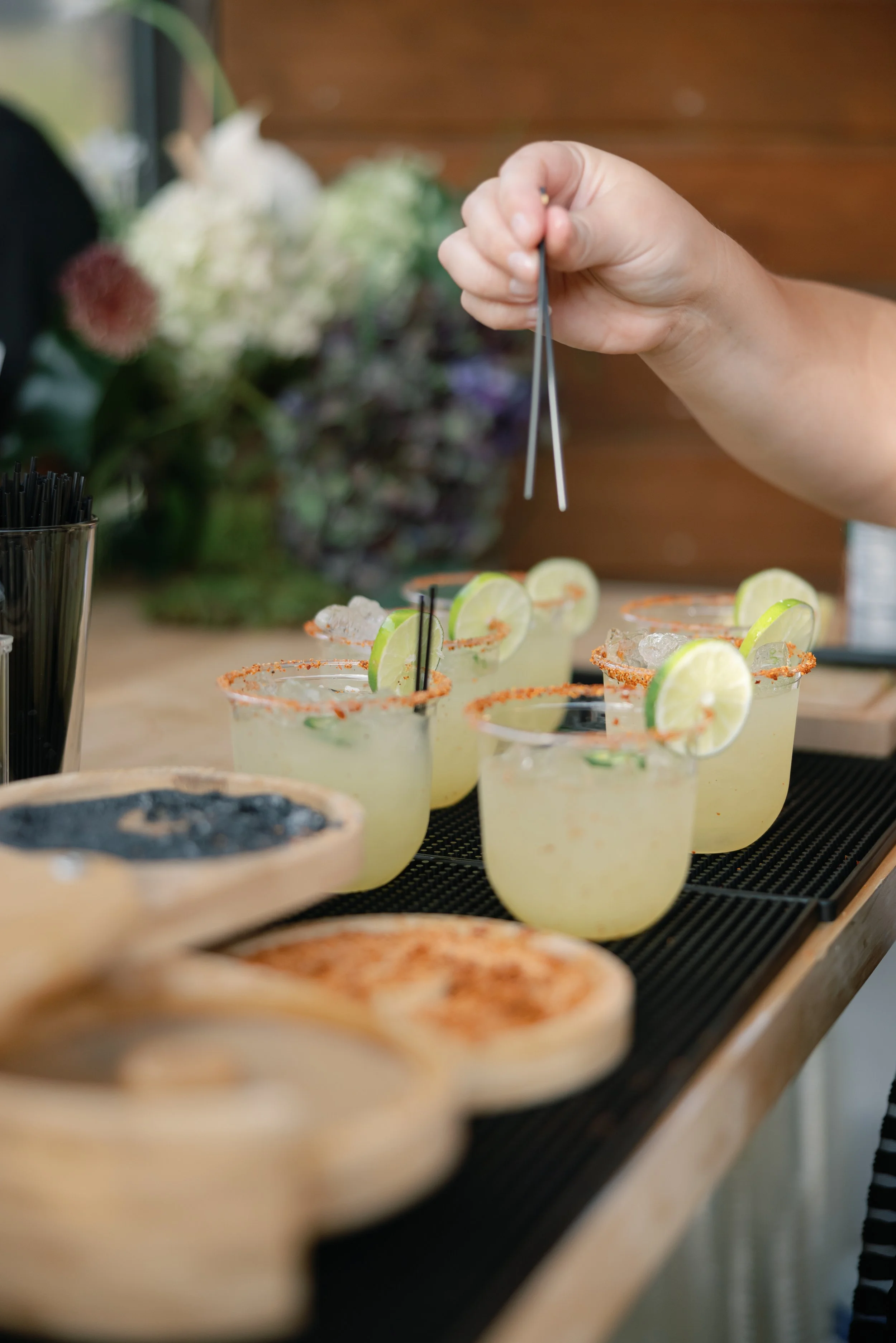Person garnishing glasses of margaritas with lime slices at a bar or restaurant.