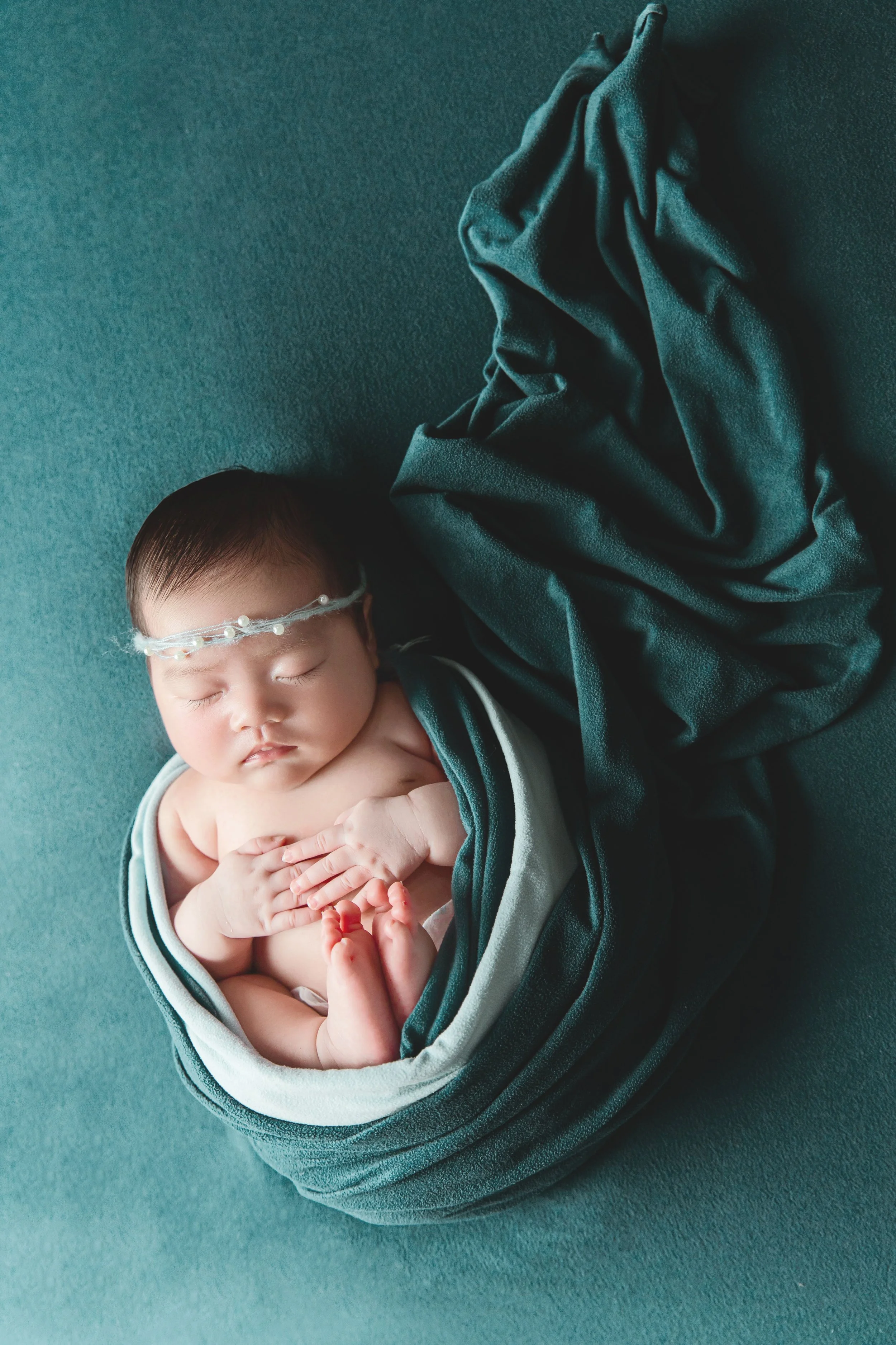 Sleeping newborn wrapped in deep teal blankets