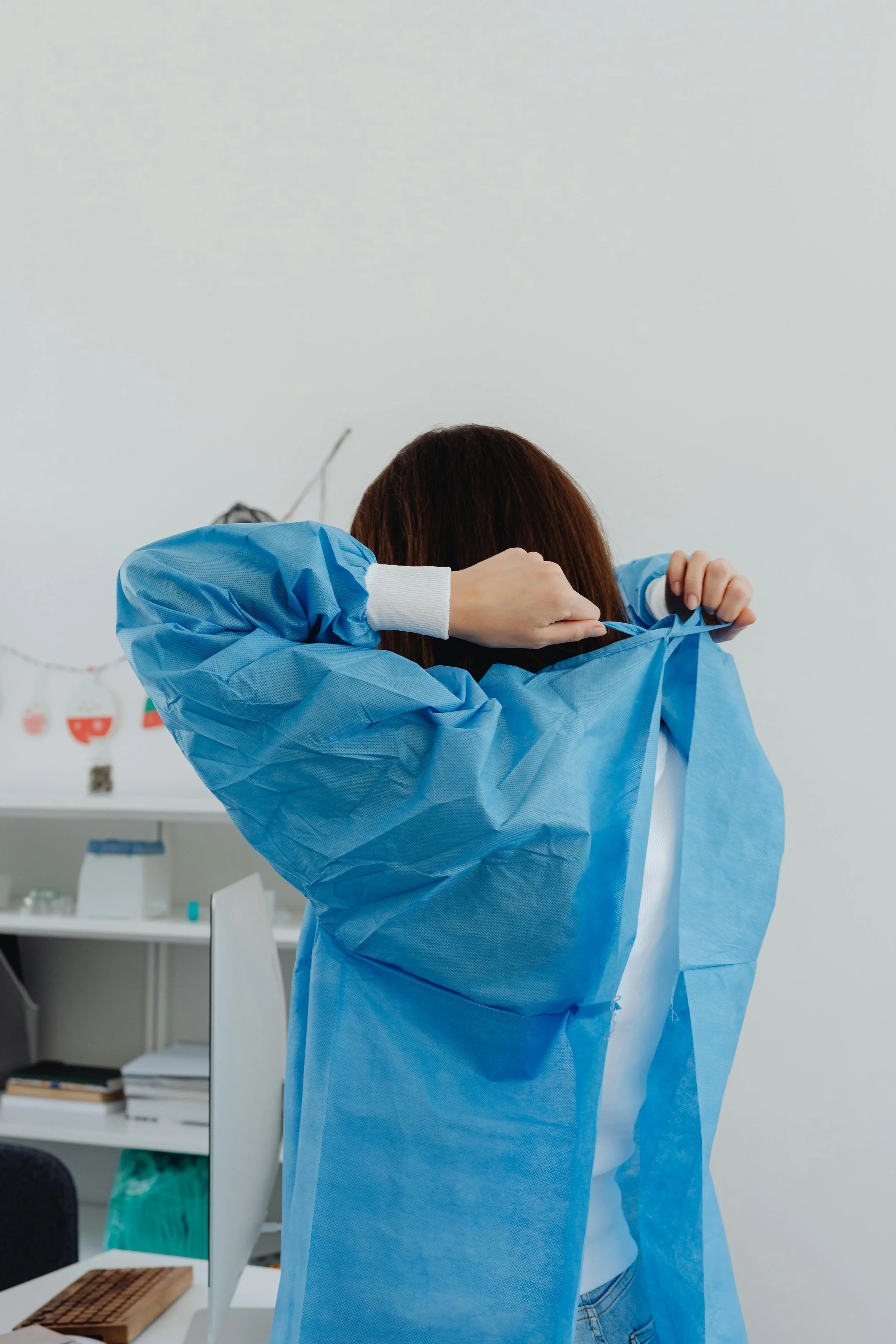 A person adjusting their blue medical gown in a clinical or laboratory setting.