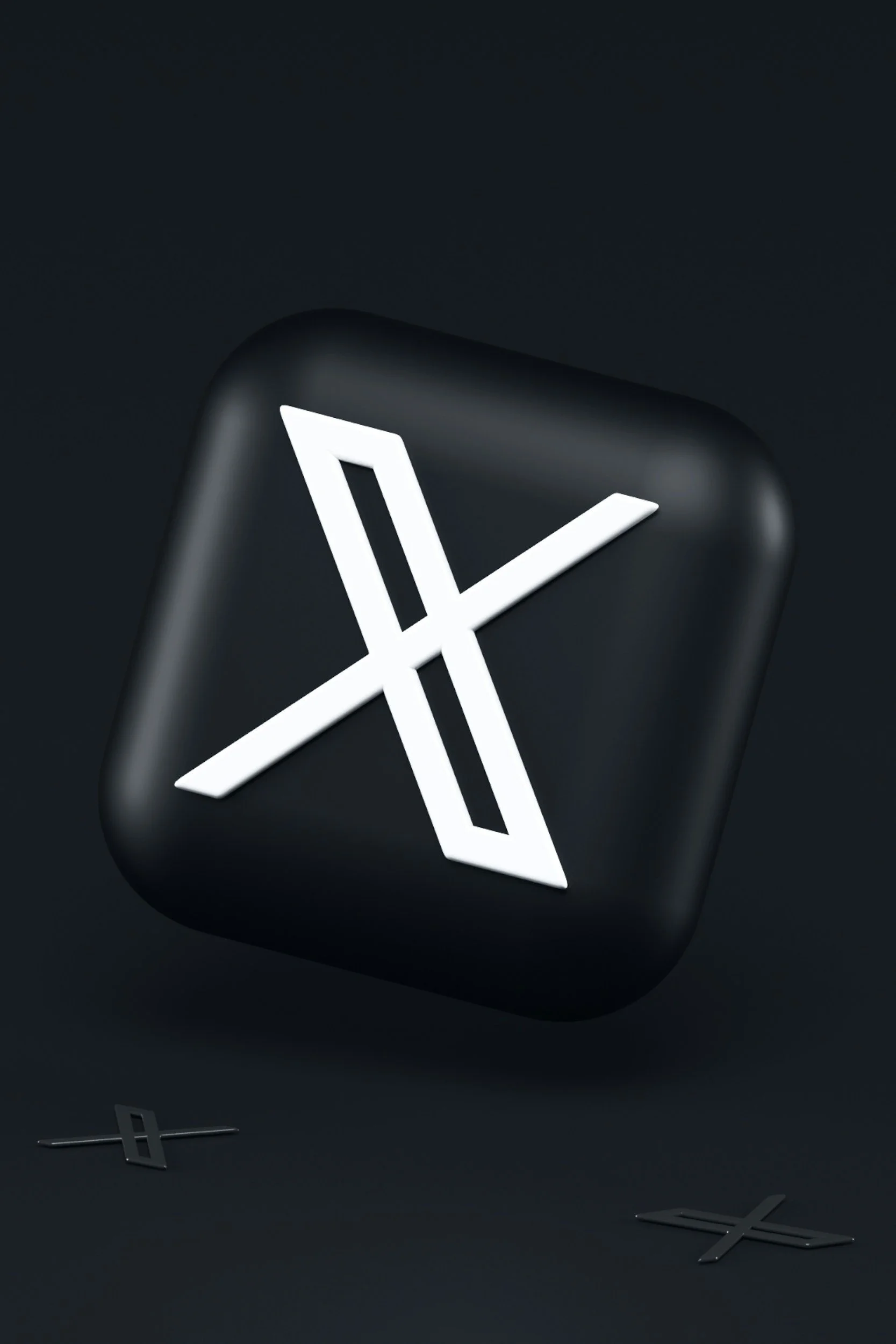 A black square-shaped device with a glowing white 'X' symbol on it, set against a dark background. Two small, similar 'X' symbols are on the surface below the device.