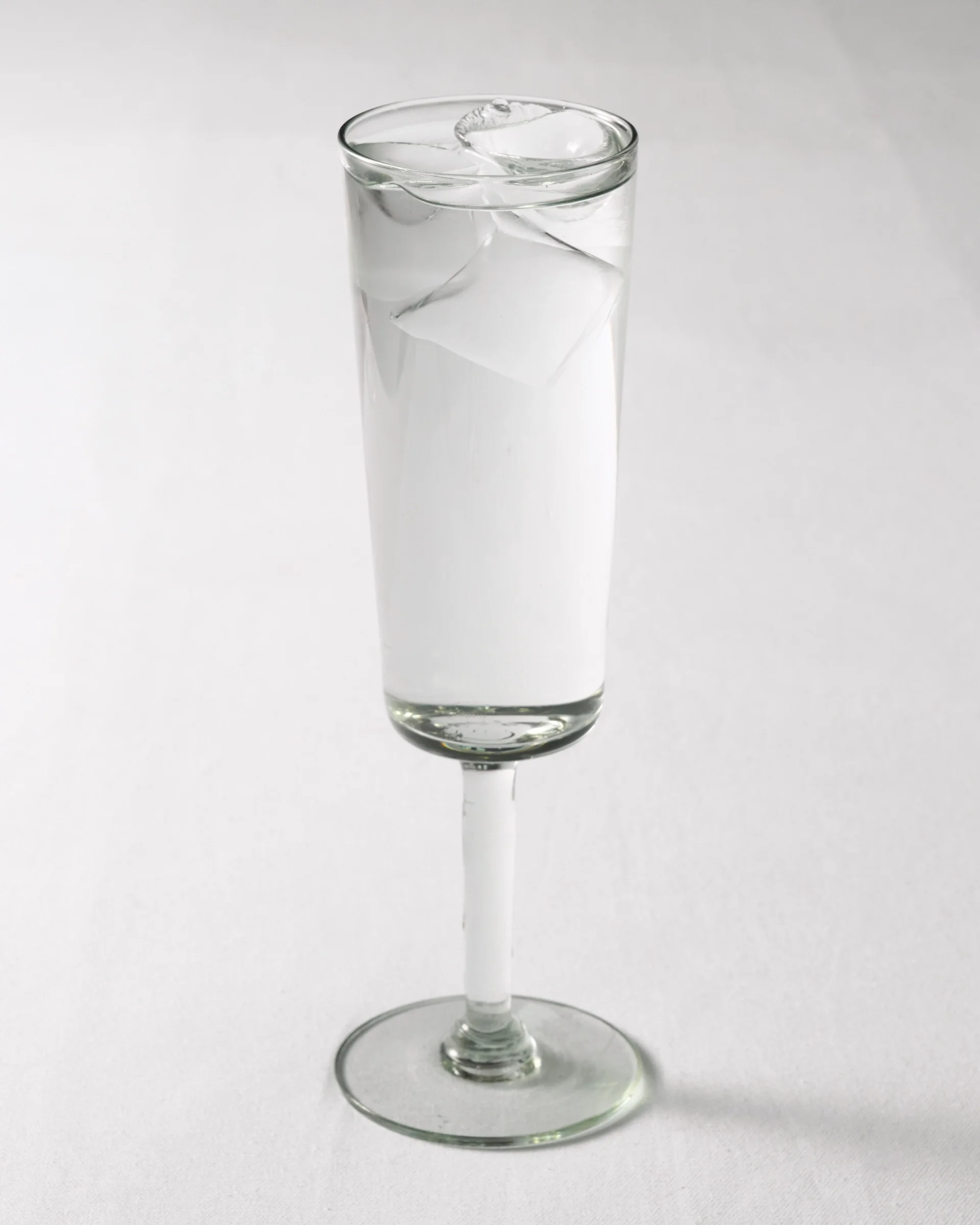 a single tall, slender stemmed glass filled with water and ice cubes
