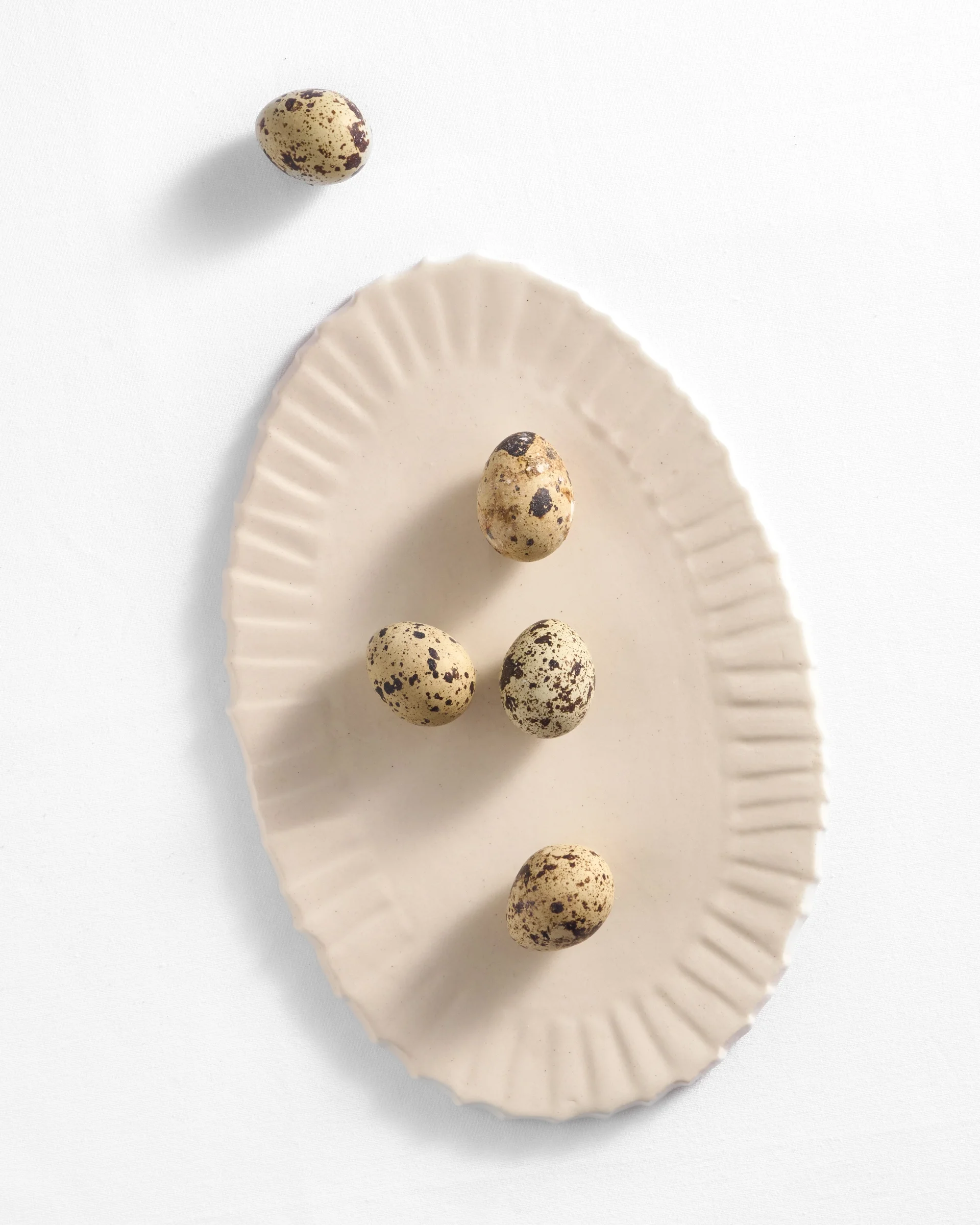 a top-down view of an oval ruffled platter holding several speckled quail eggs against a white surface