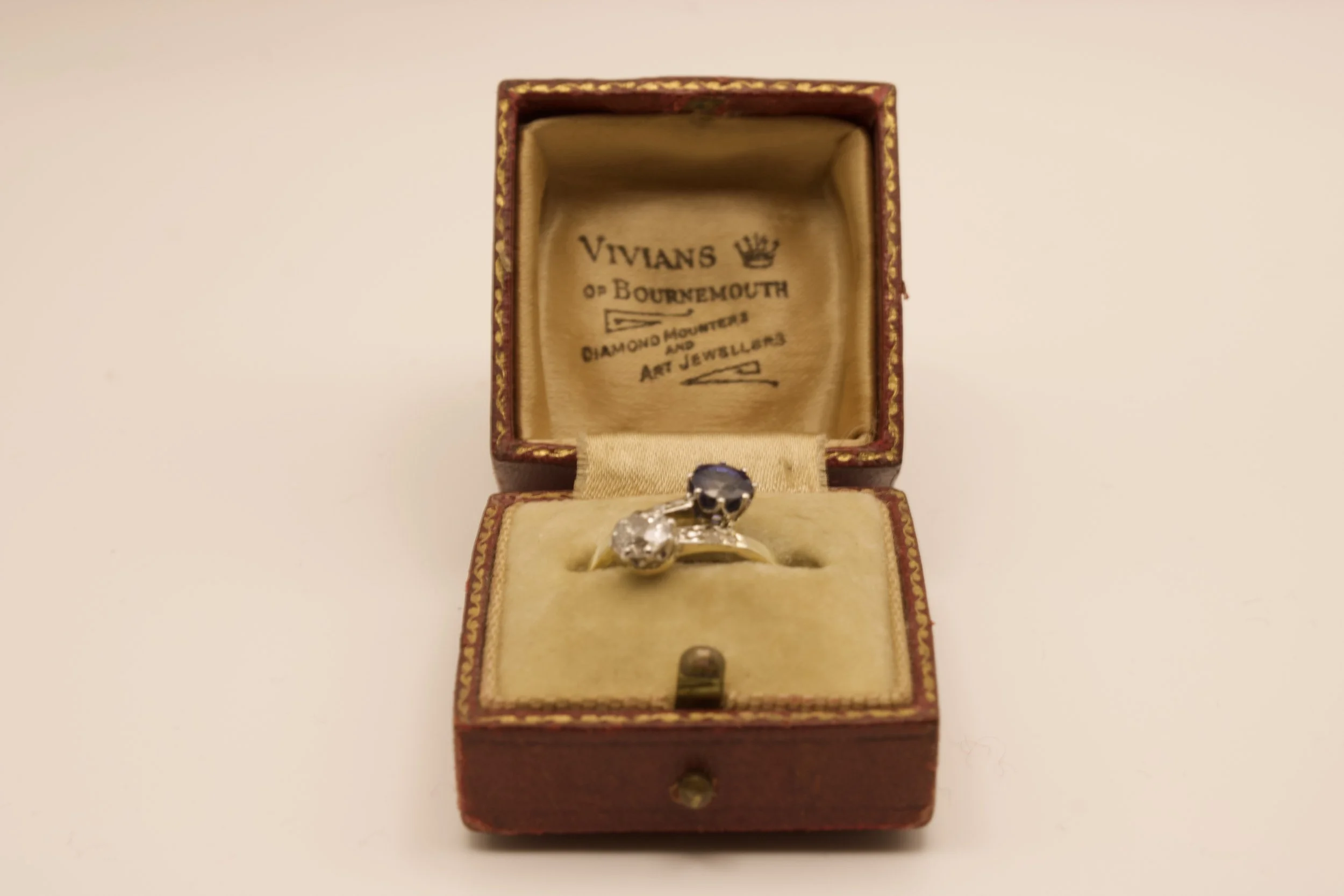 Vintage jewelry box with a ring inside, featuring two stones, one black and one clear, on a cushioned interior.