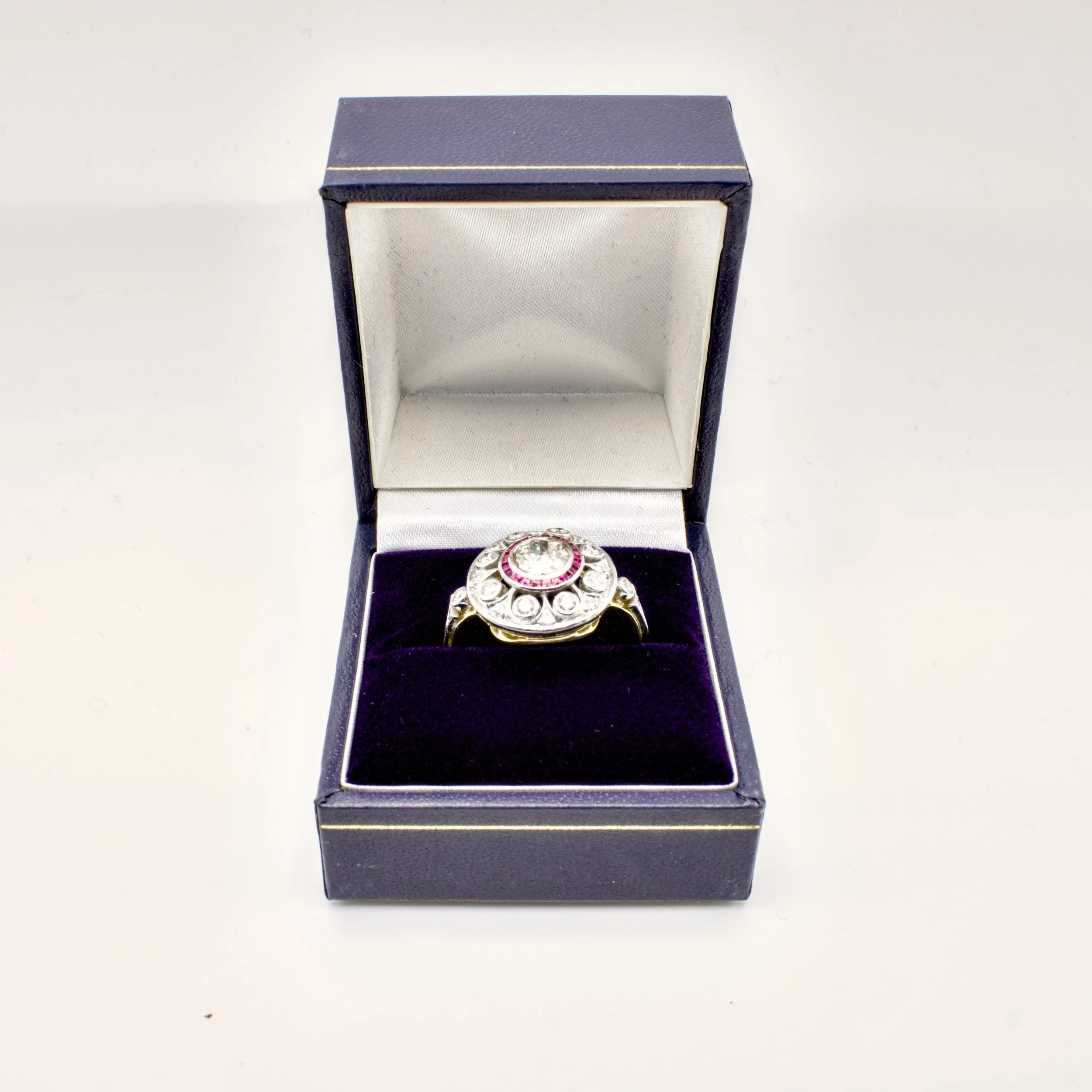 An open navy blue jewelry box with a decorative ring inside, placed on a plain surface.
