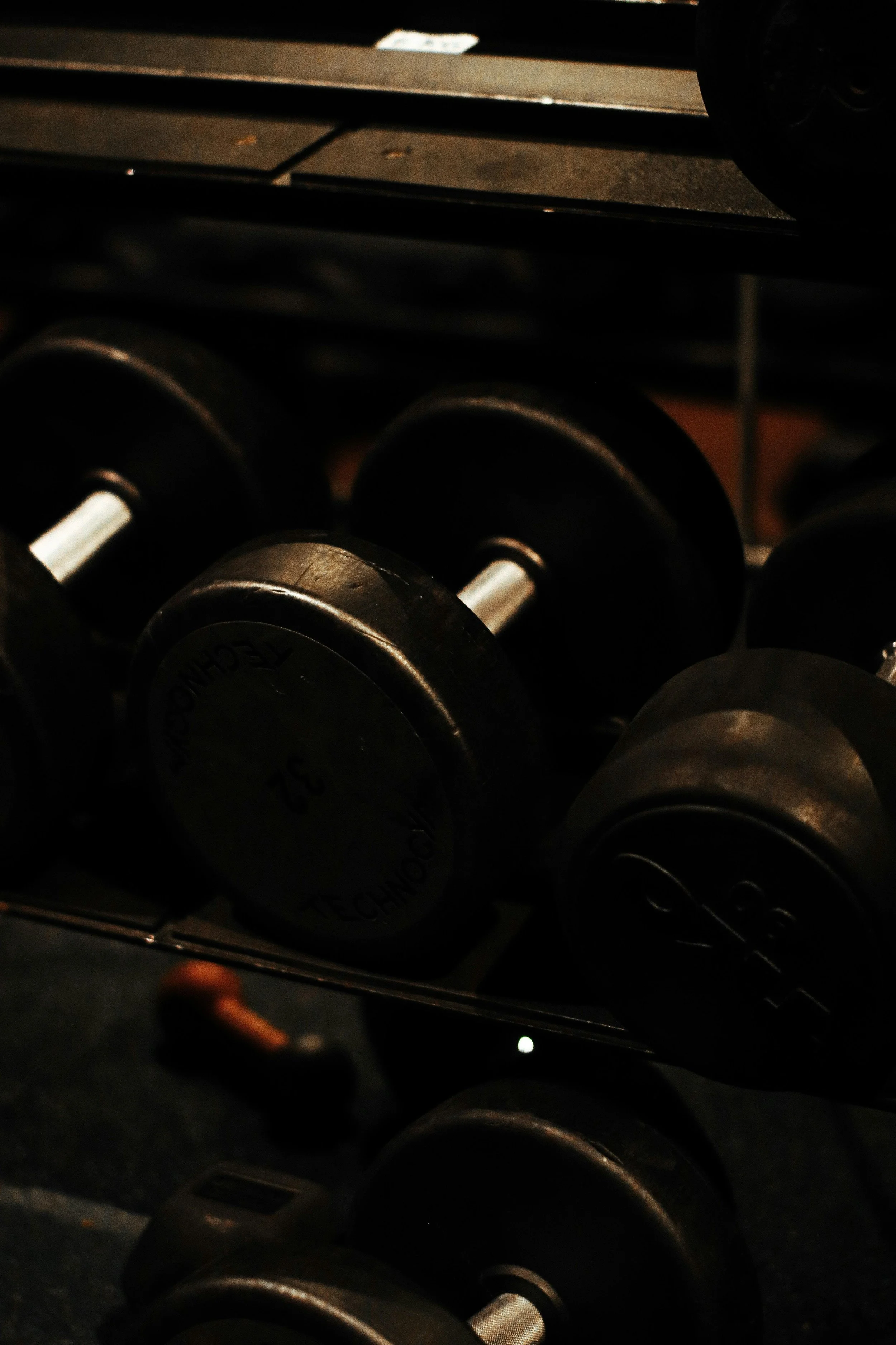 A rack of black dumbbells in a gym, with a dark background.