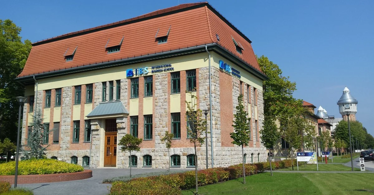 Building with signs for International Business School (IBS) surrounded by trees and a well-kept lawn under a blue sky.
