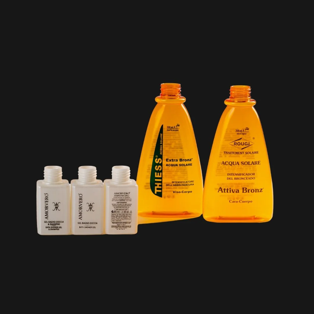 Three bottles of shower gel and shampoo from the brand Amwerò, and two bottles of tanning lotion from the brand Rouge, labeled for sun protection and tanning enhancement, against a black background.