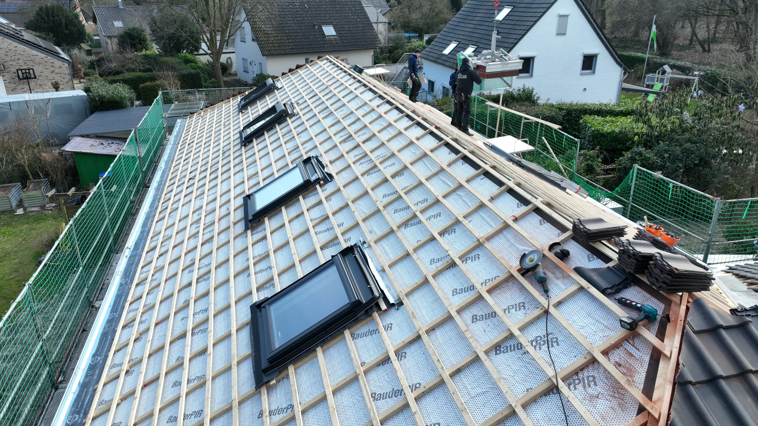 Auf einem Hausdach wird eine Dachsanierung mit neuen Dachfenstern durchgeführt. 