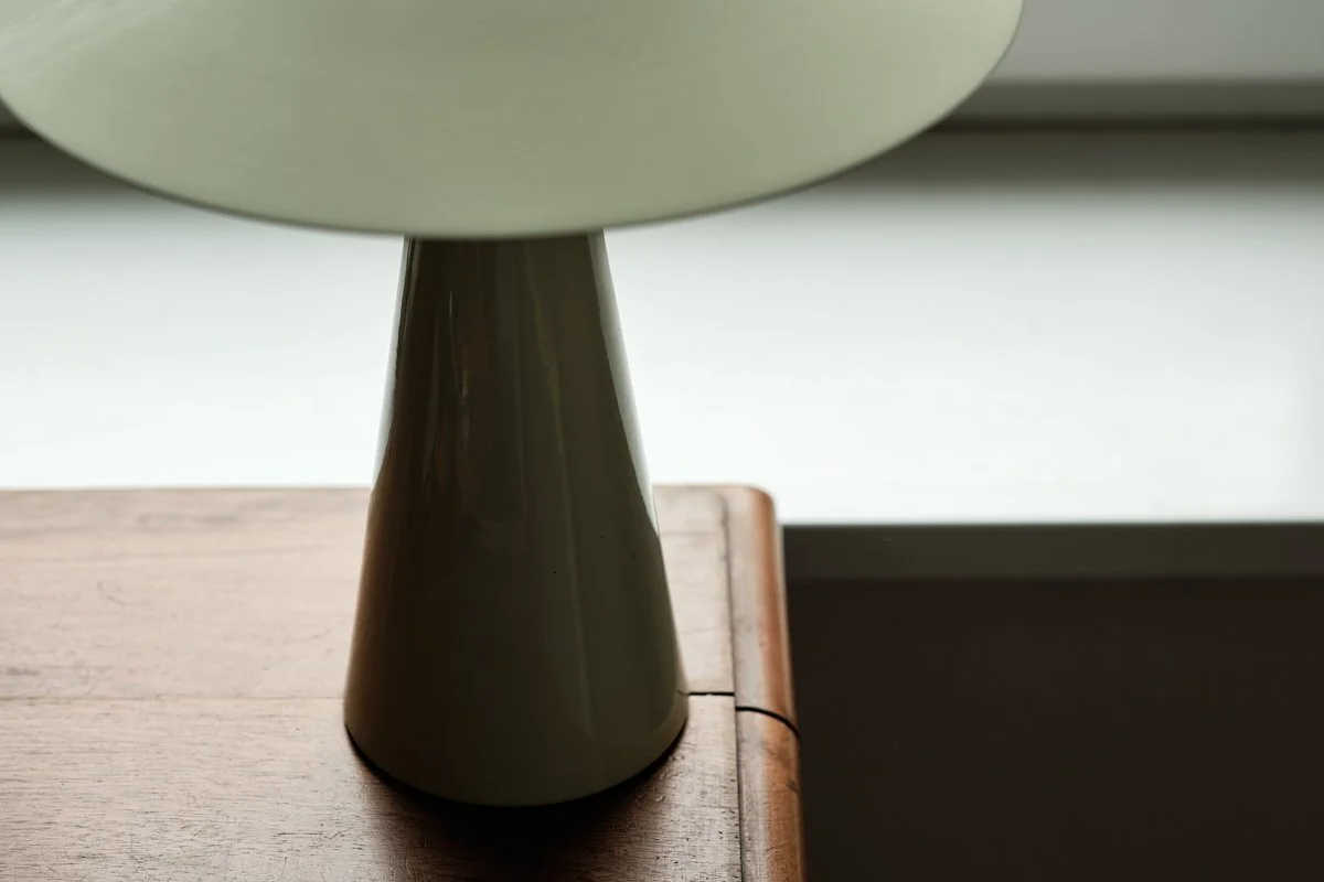 Nahaufnahme eines runden, hellgrünen Tellers auf einem dunklen, konischen Sockel, der auf einem Holztisch steht.