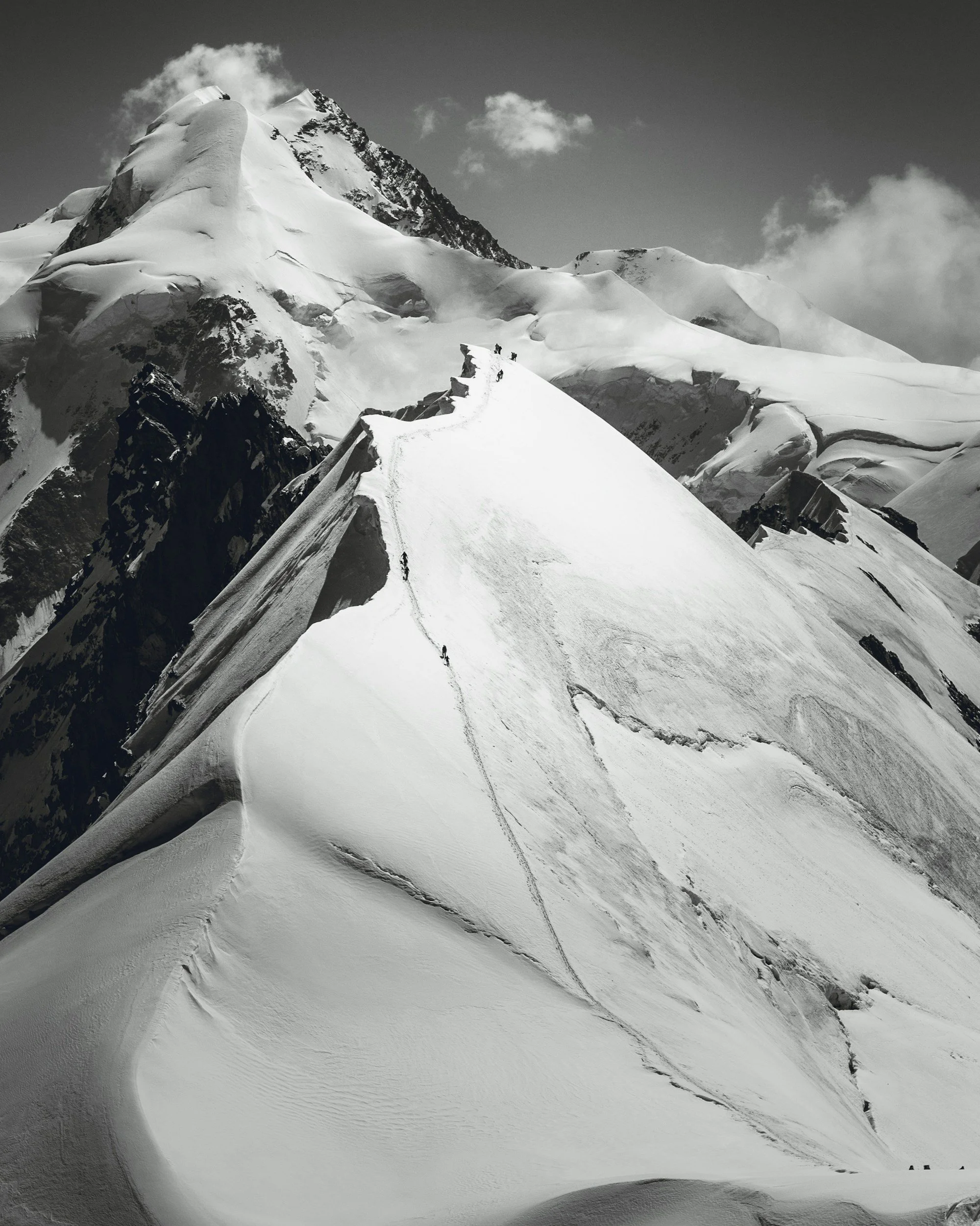 Black and white mountaineers walking along a narrow alpine summit ridge