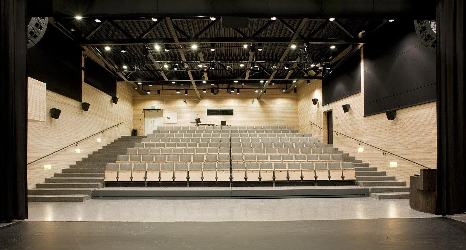 Tomt auditorium med lenestoler, trappetrinn og lys, sett fra scenen.