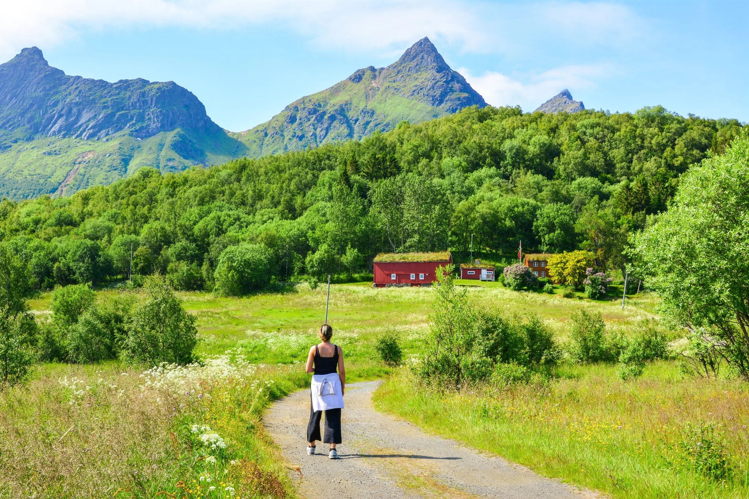 Person som går på en grusvei i et grønt landskap med fjell i bakgrunnen.