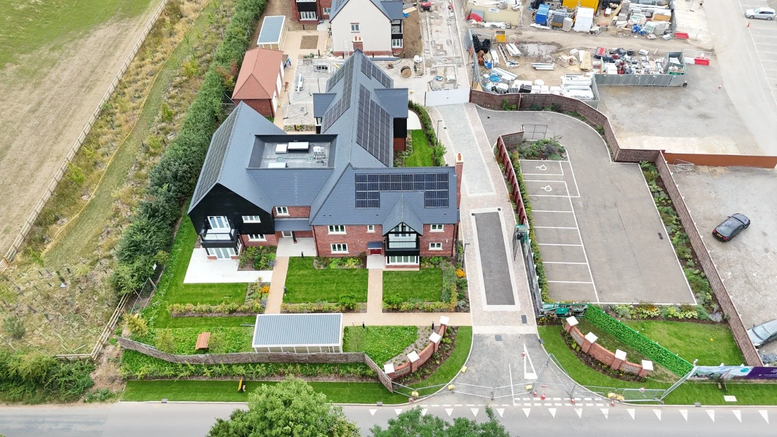 Aerial view of a modern residential house with a well-maintained garden, parking lot, and surrounding construction site.