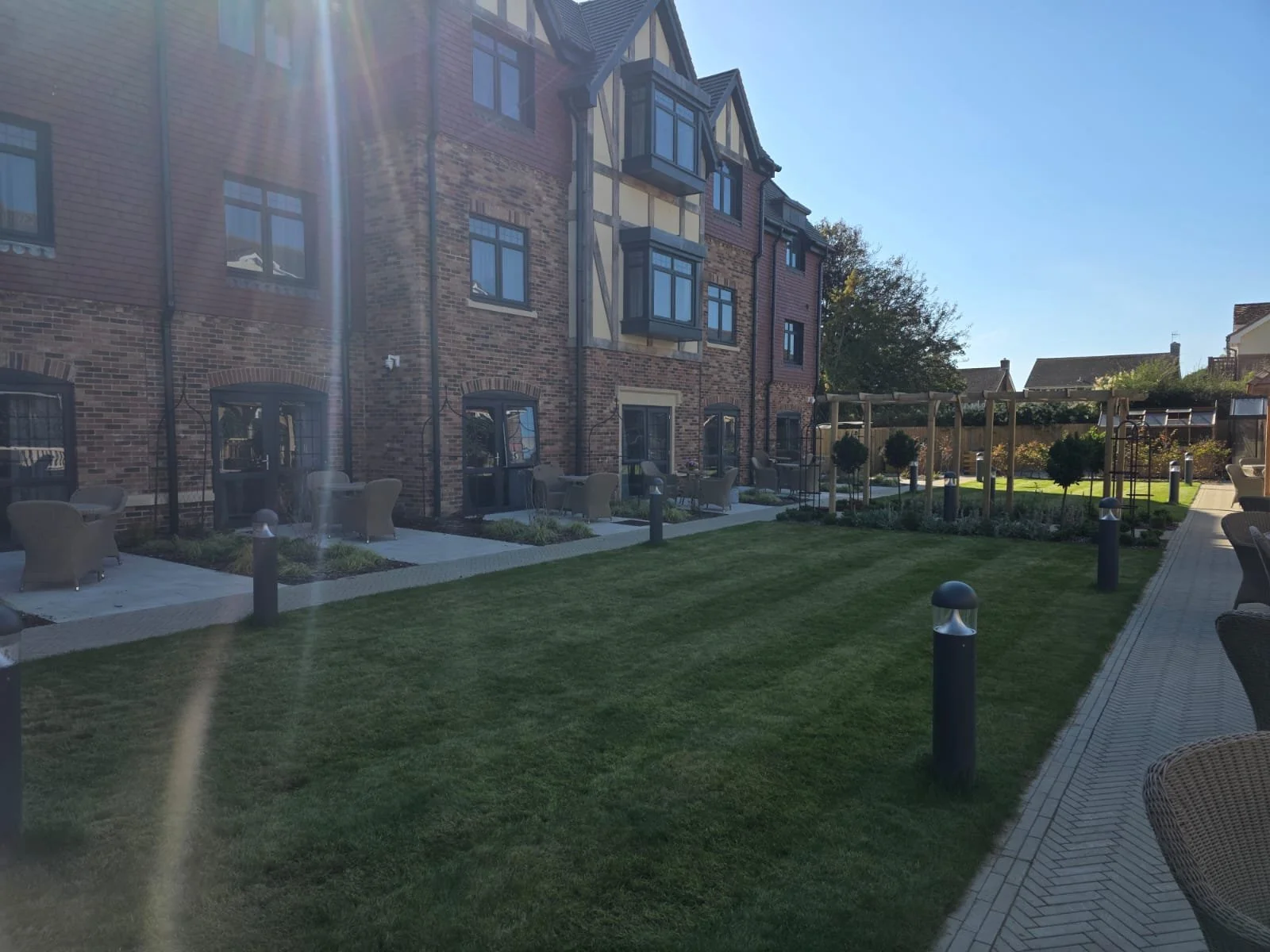 A residential courtyard with a grassy area, outdoor seating, small trees, and a brick building with multiple windows.