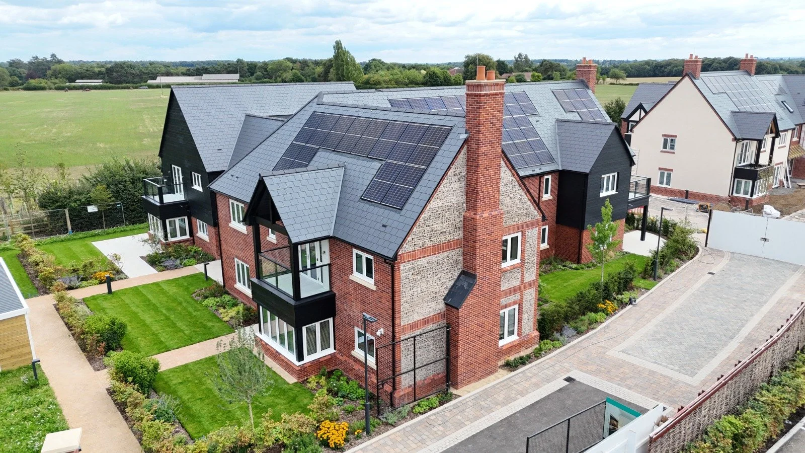 Aerial view of a modern brick and black wood house with solar panels on the roof in a suburban neighborhood.