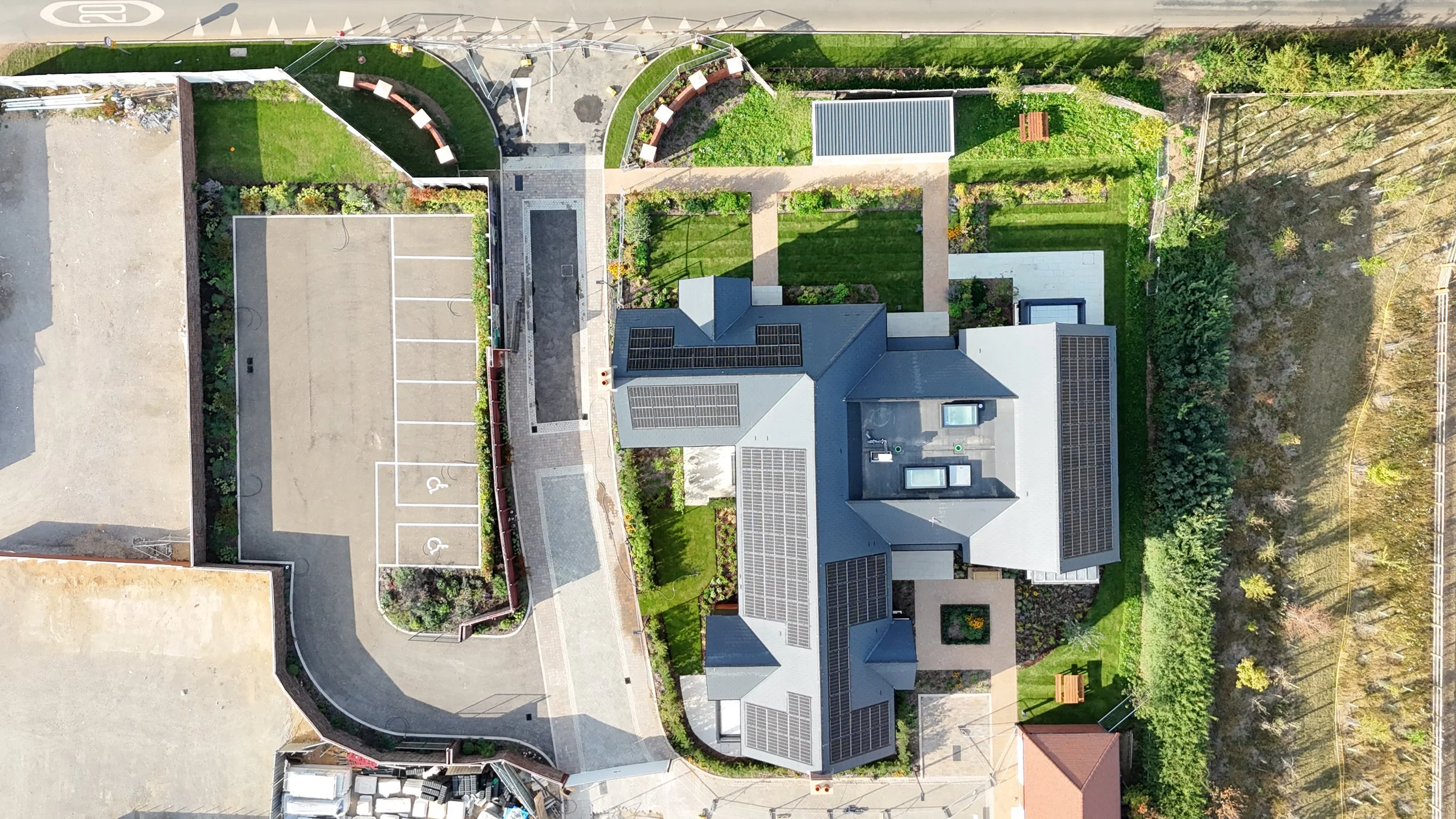 Aerial view of a residential property with solar panels on the roof, surrounded by a garden and various pathways.