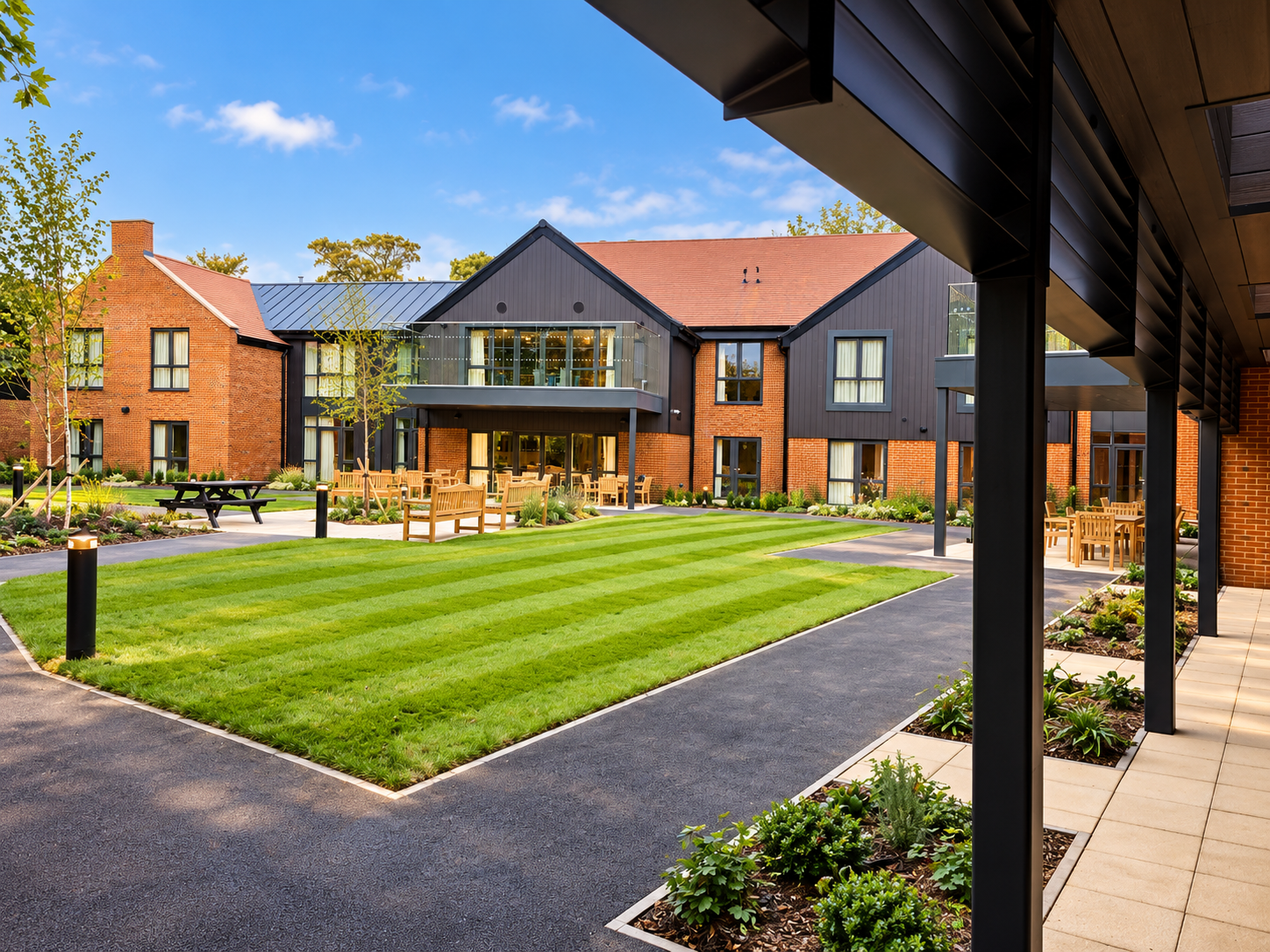 Modern residential or communal building with a well-maintained lawn, outdoor seating, and greenery.