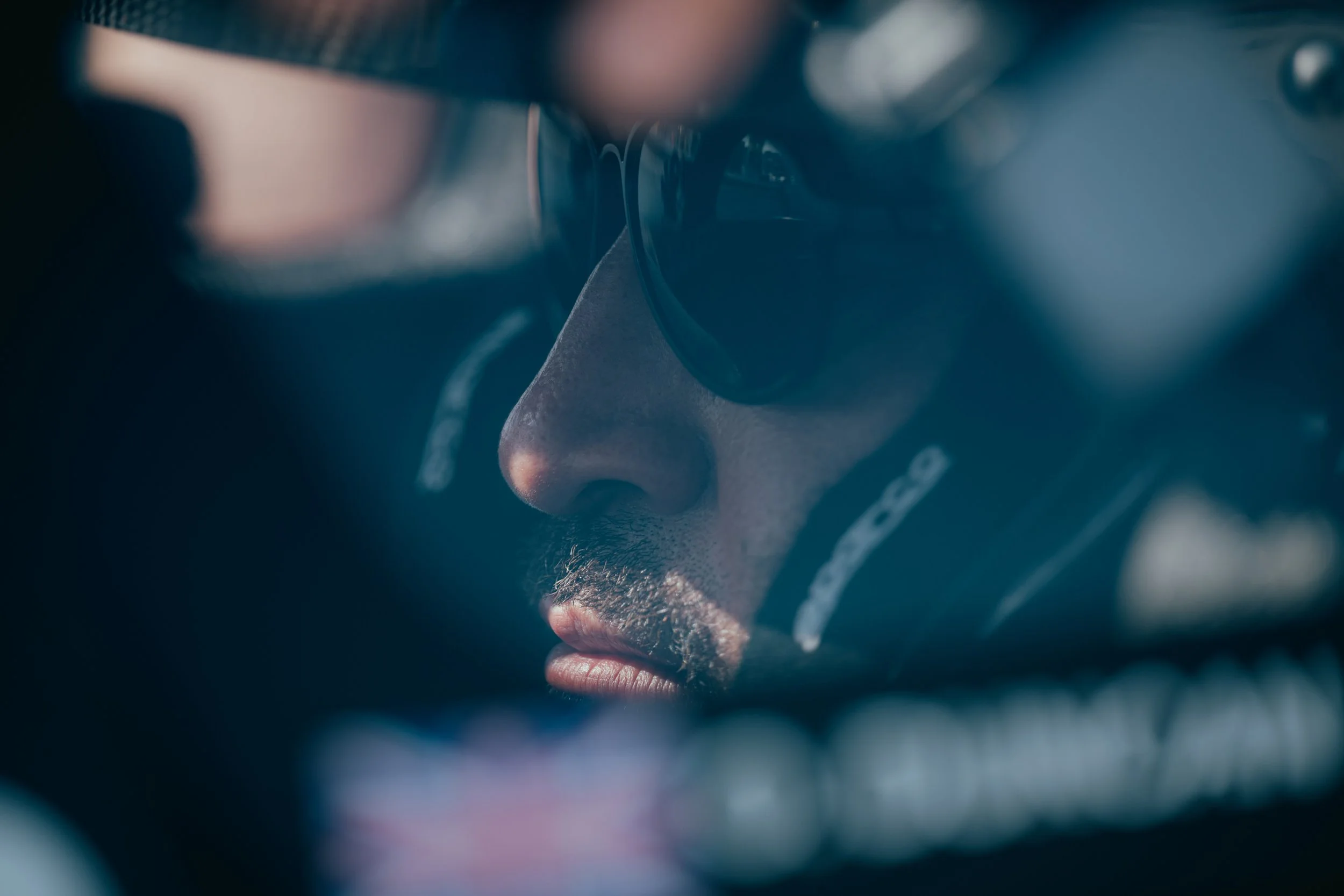 Close-up side view of a man with a beard and earrings wearing a red Ferrari racing jacket, against a red background.