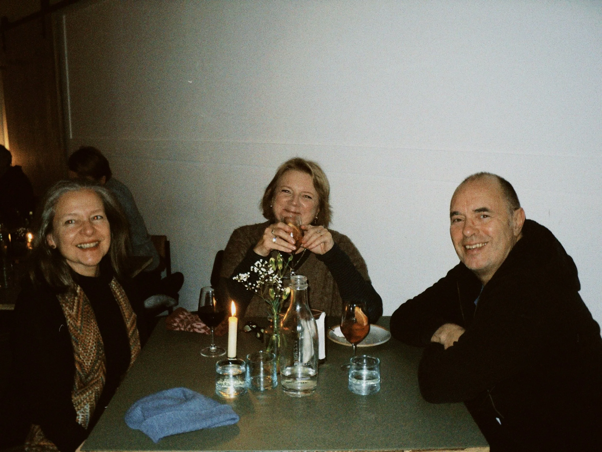 People gathered at a dinner table celebrating, with a candle, flowers and drinks, smiling and enjoying themselves.
