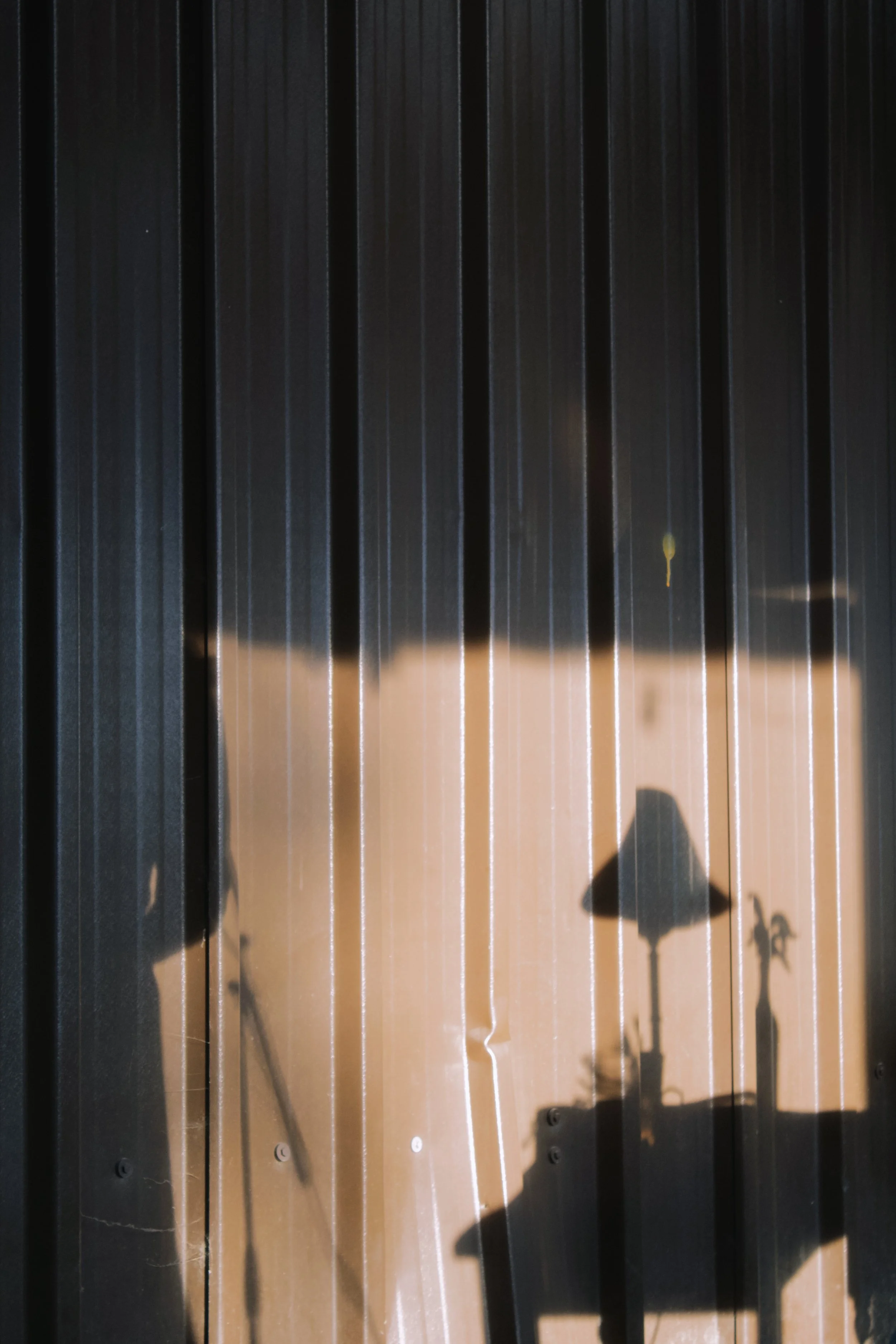 Shadow of a person and person on bicycle cast on a metal surface with vertical lines and a small, yellowish spot.