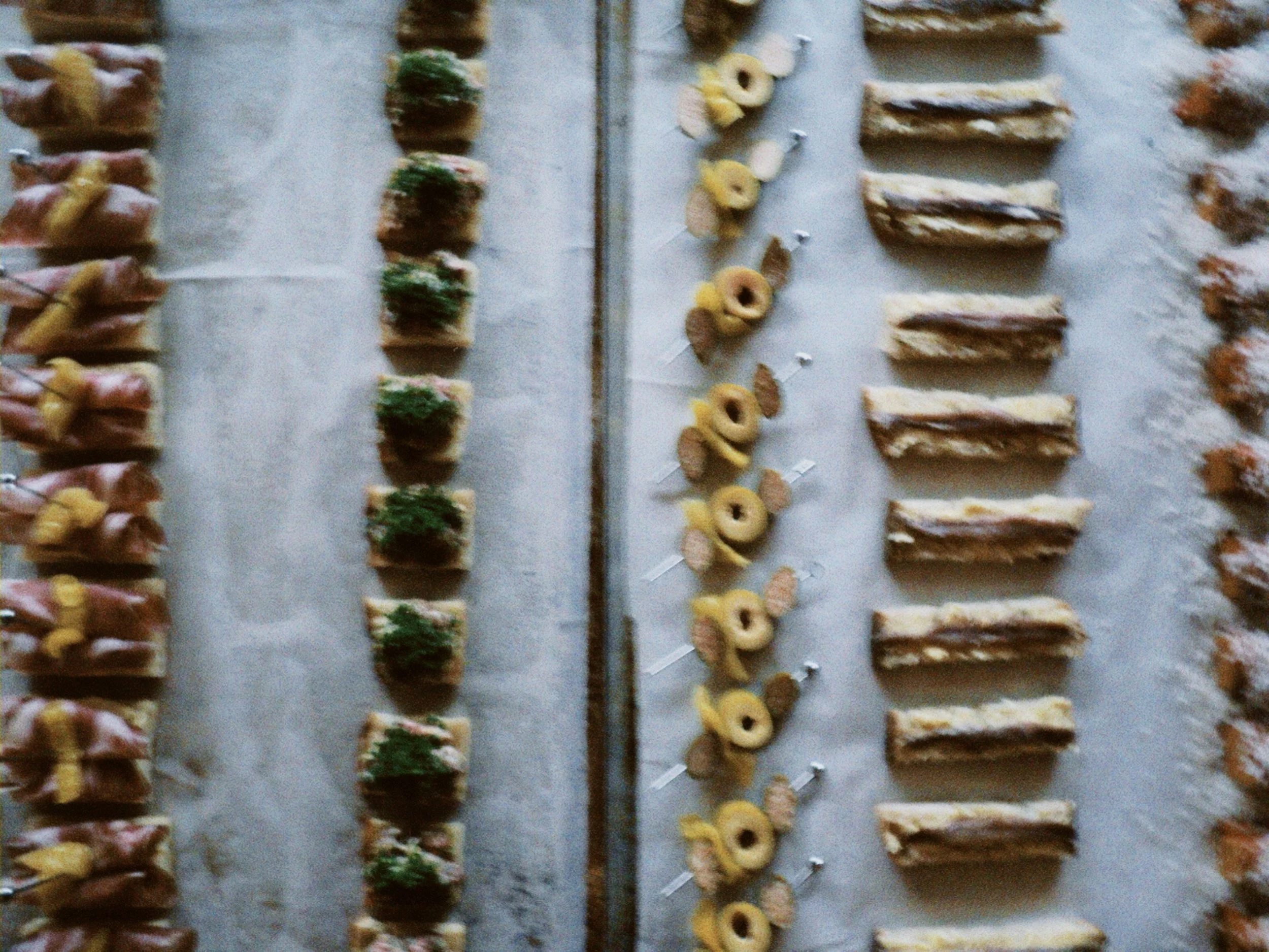 Multiple rows of various pastries and baked goods arranged on a flat surface, including pastries with fruit and toppings, and different types of cookies.