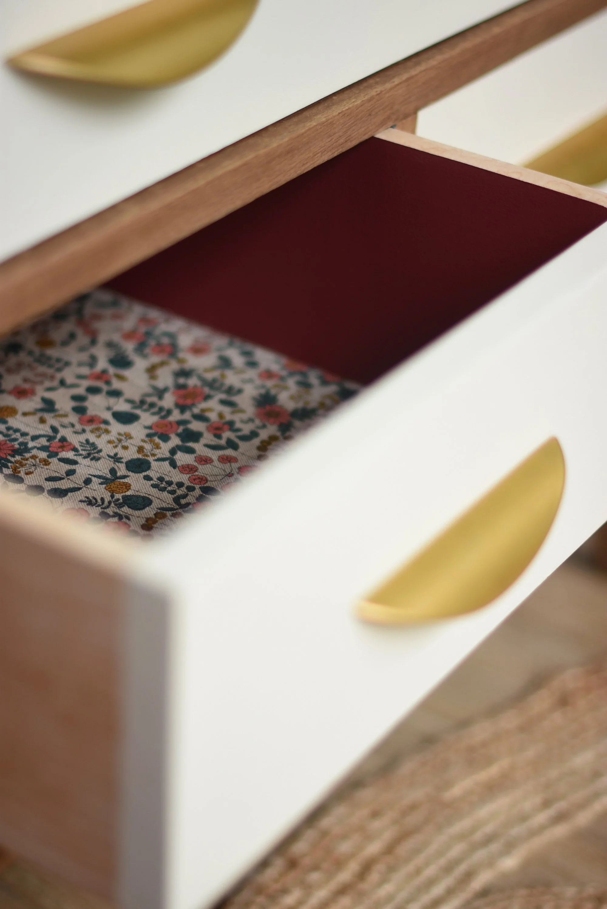 Un tiroir de commode blanc avec une poignée jaune, ouvert pour révéler un intérieur en bois rouge et une nappe à motifs floraux.